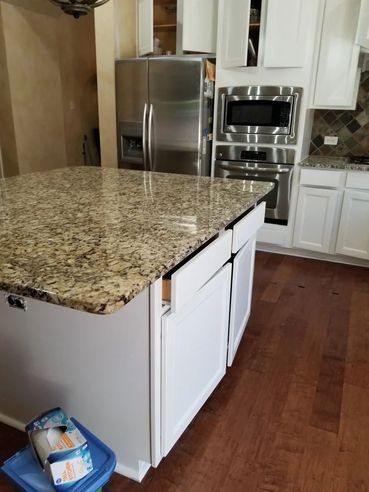 Kitchen island with granite countertop, white cabinets, stainless steel appliances.