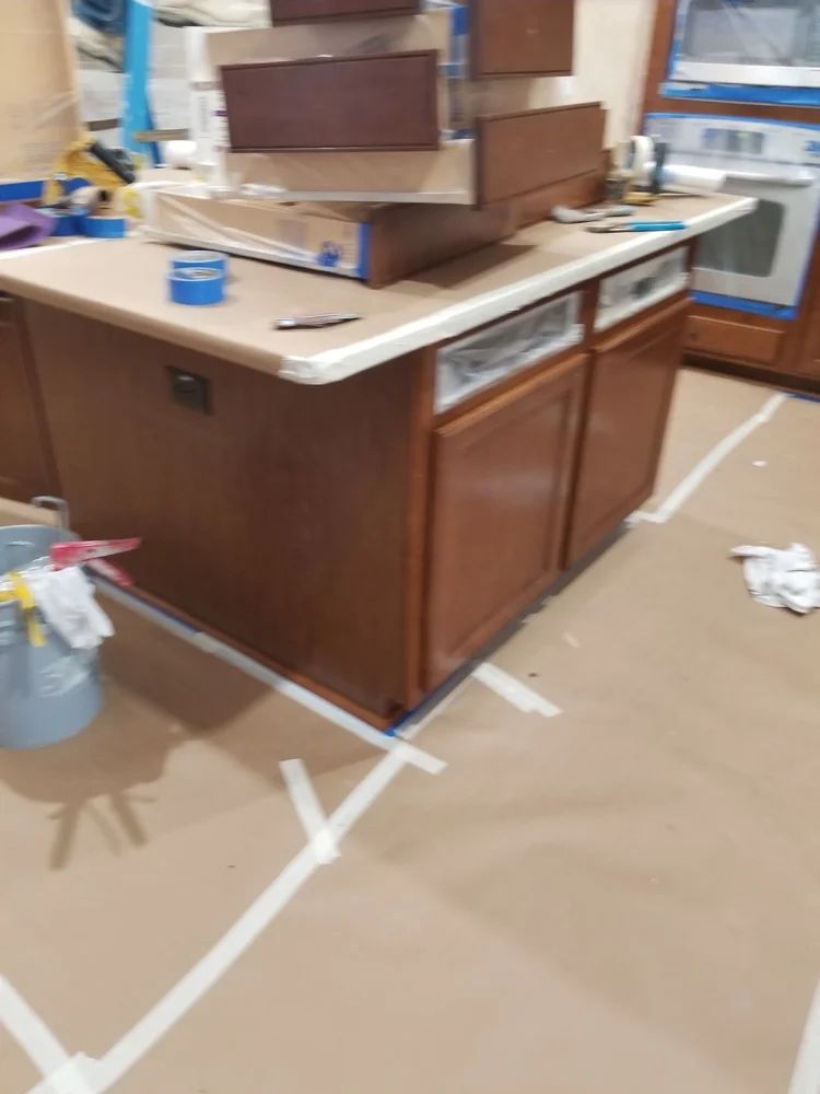 Kitchen island with brown cabinets being prepped for painting, floor taped off.