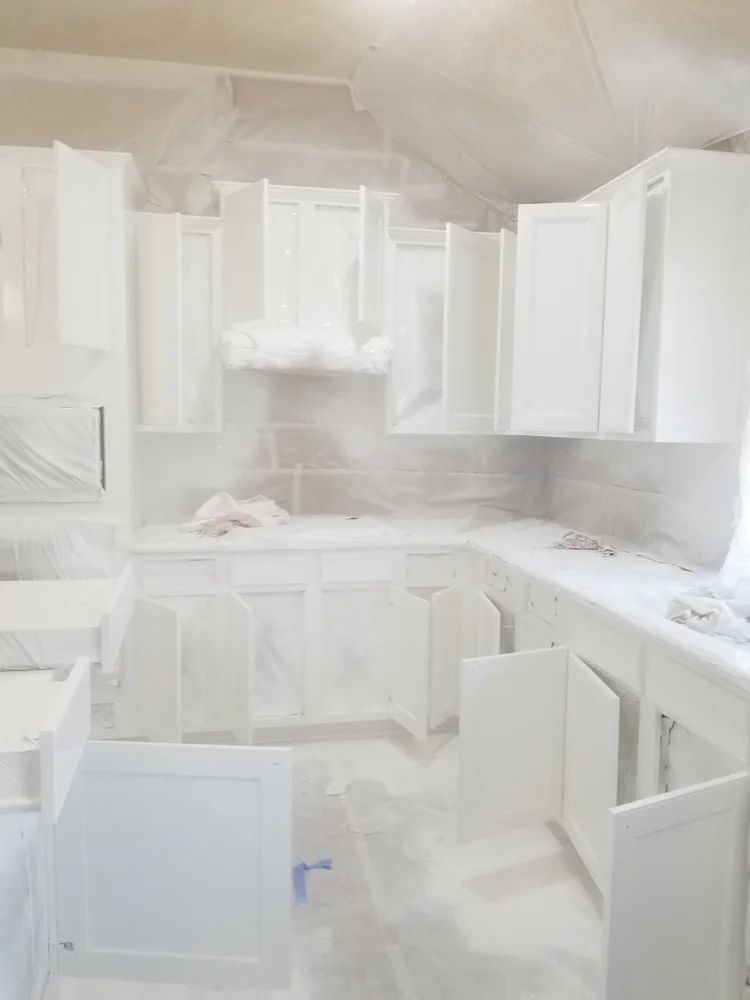 Kitchen cabinets, drawers, and countertops covered in plastic, likely for painting. White.