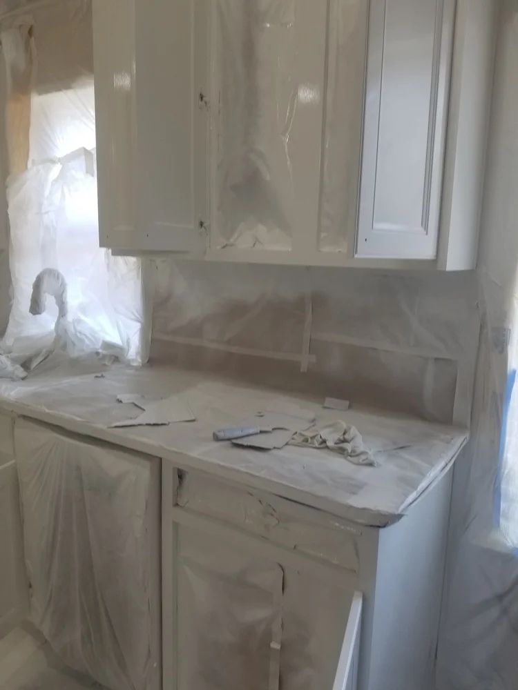 Kitchen cabinets and countertop covered in white paint, prepared for painting. Sink visible.