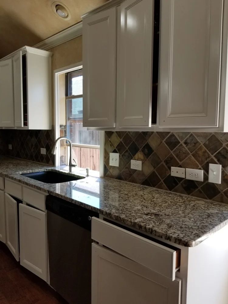 Kitchen with white cabinets, granite countertop, and diamond-patterned backsplash; stainless steel sink and appliances.