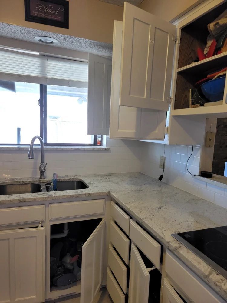 White kitchen cabinets with granite countertop, sink, and open cabinet doors.