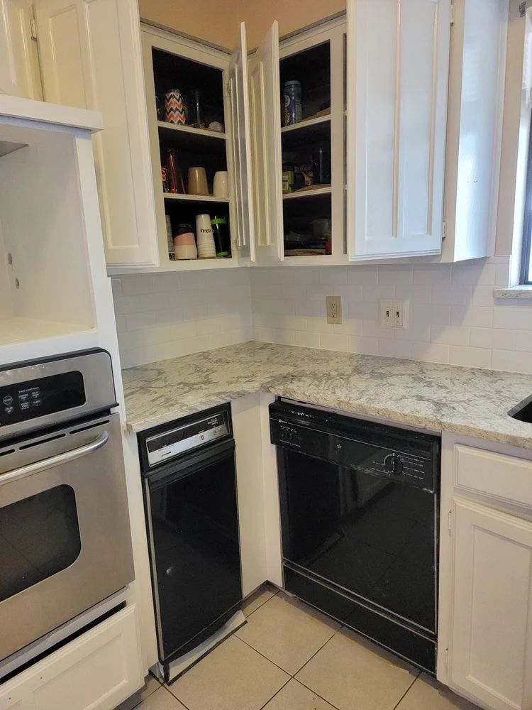 Kitchen corner with white cabinets, light countertop, black dishwasher and oven.