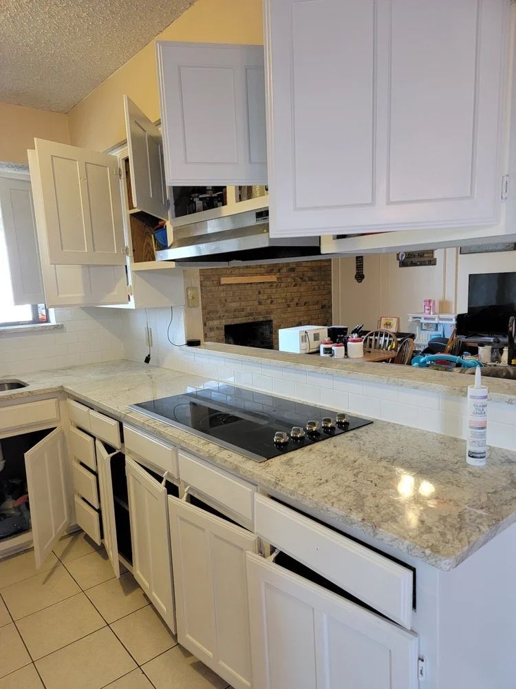 White kitchen cabinets with granite countertop, electric cooktop, and opened doors.