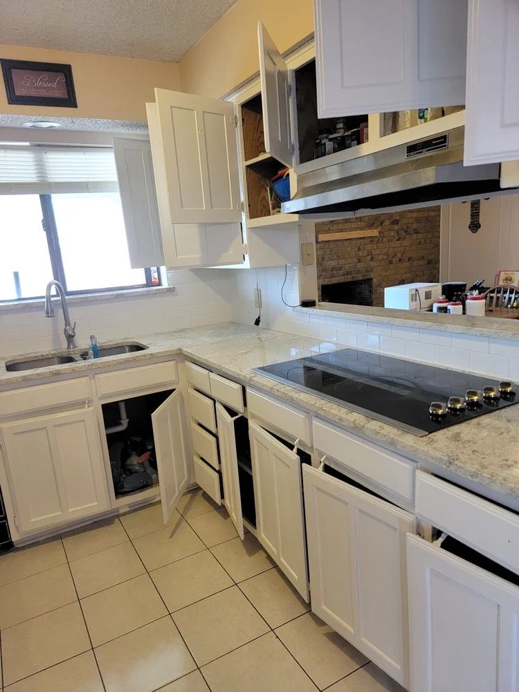 White kitchen cabinets with open doors, countertop, sink, and stovetop.