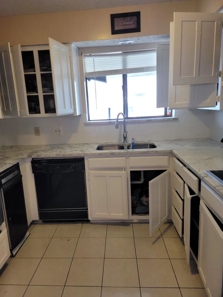 White kitchen cabinets, black appliances, a sink, and a window with blinds.