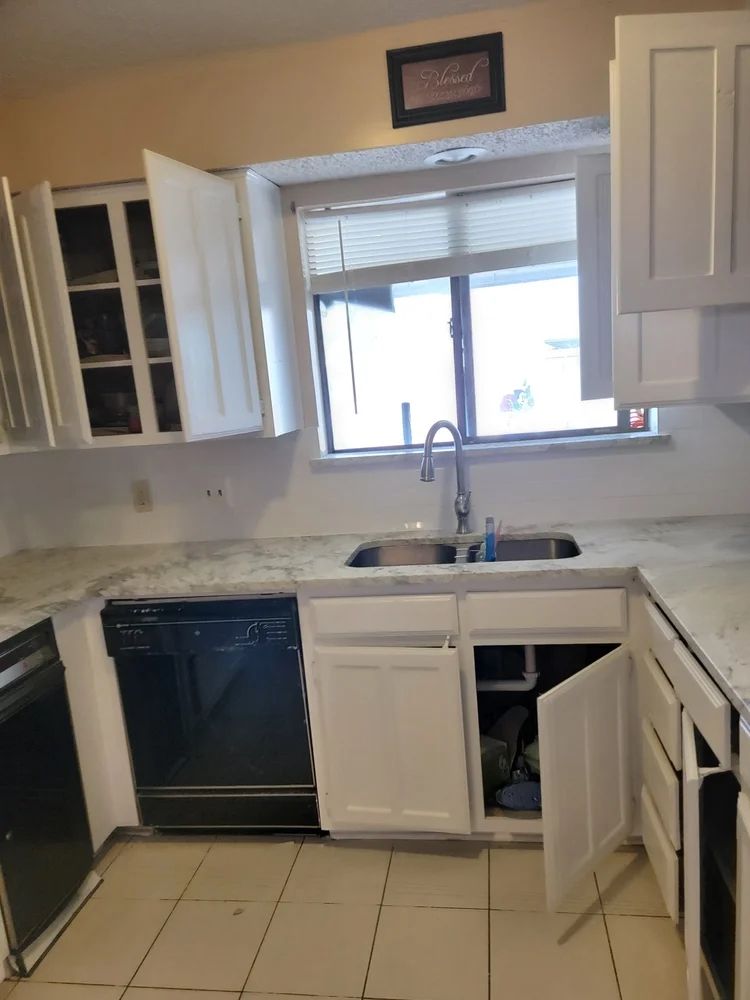 White kitchen cabinets, black appliances, a sink under a window, and light countertops.