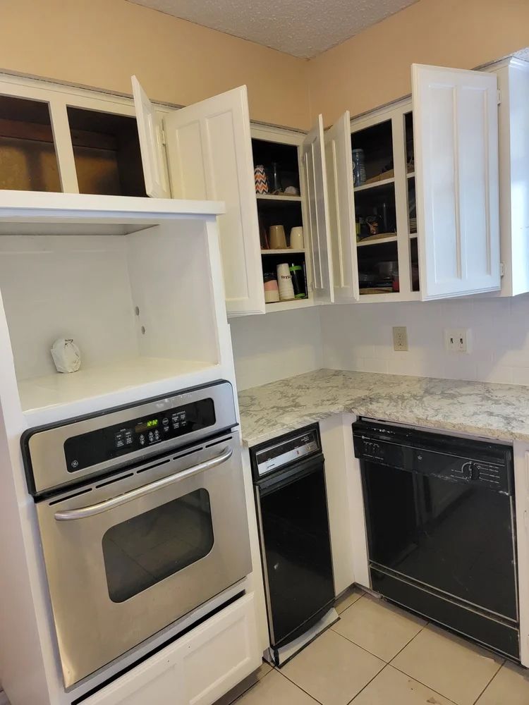 White kitchen cabinets with open doors, granite countertop, oven, and dishwasher.