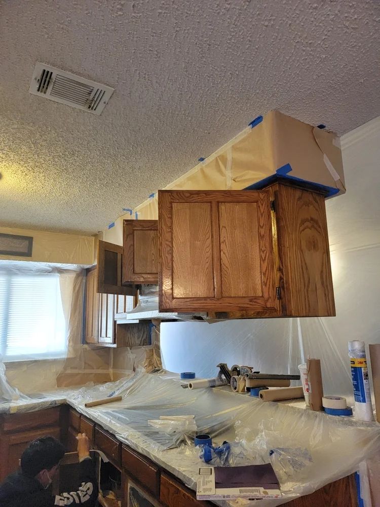 Kitchen cabinets being refinished; covered with plastic and taped for protection.