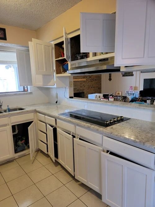 White kitchen cabinets, some open, sit against a white countertop with a stovetop.
