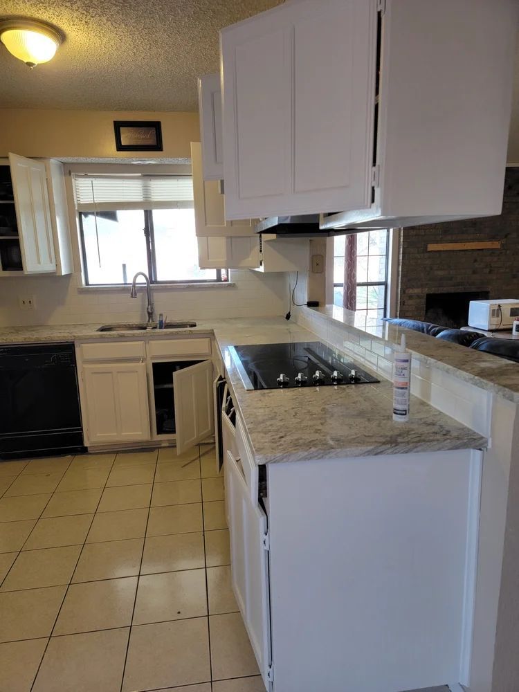 White kitchen cabinets with granite countertops, open doors, and built-in stovetop.