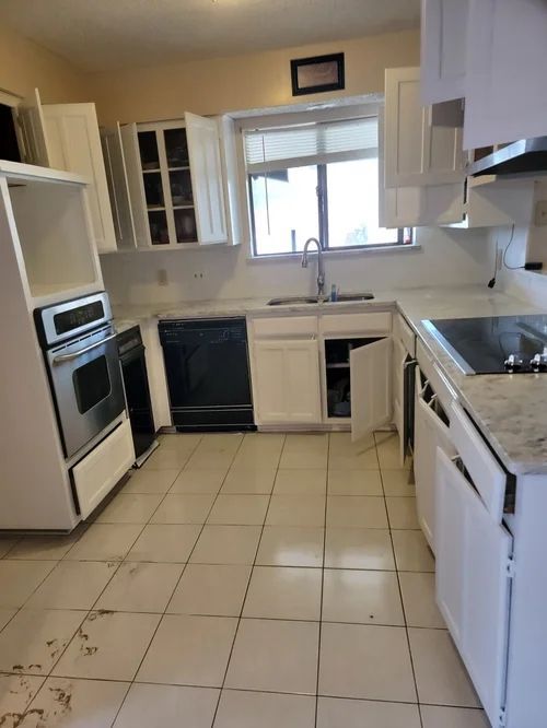 Kitchen with white cabinets, black appliances, window, and tiled floor.