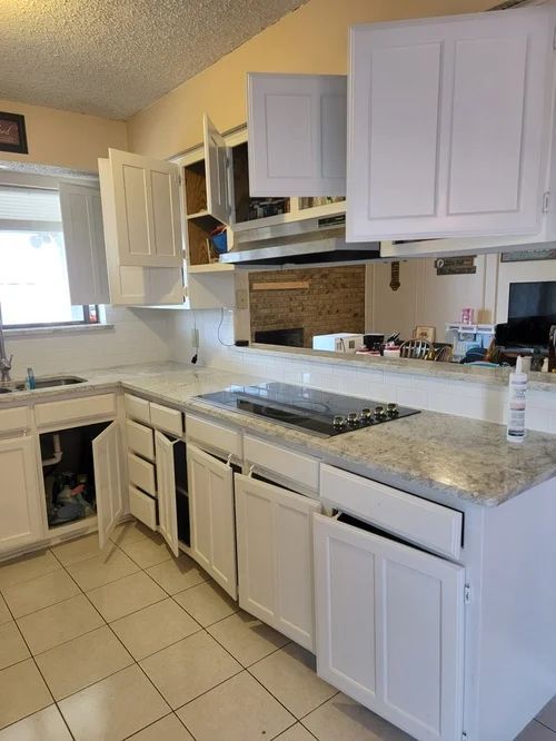White kitchen cabinets with doors open, countertop, stove, and a window.