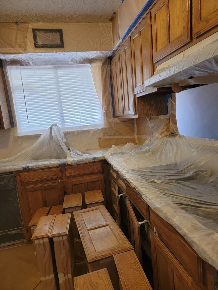Kitchen cabinets being refinished; wood cabinets, covered countertops and walls, taped and plastic sheeting.