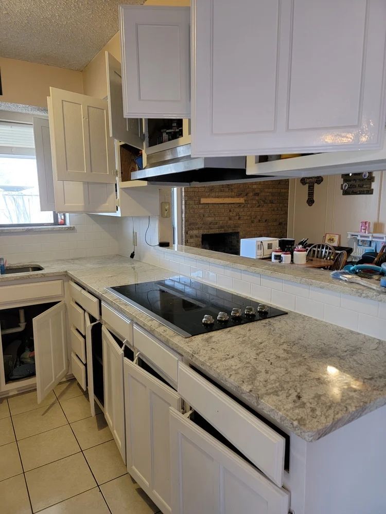 Kitchen with white cabinets, light countertops, and an electric cooktop. The cabinets and doors are open.
