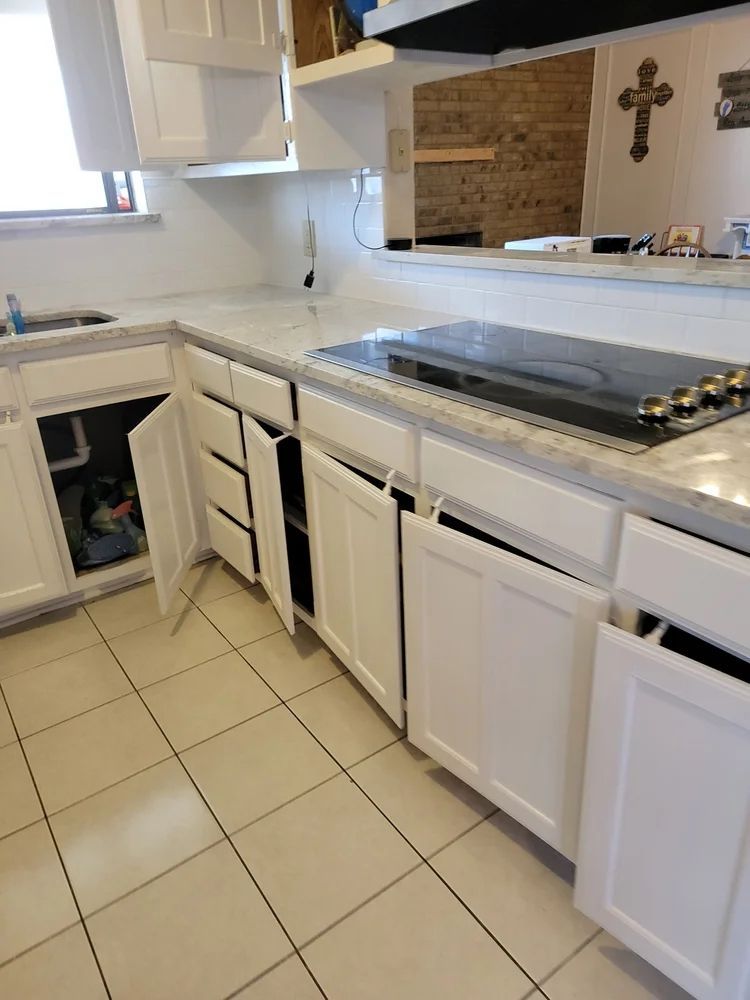 White kitchen cabinets with open doors, granite countertop, stovetop, and tiled floor.