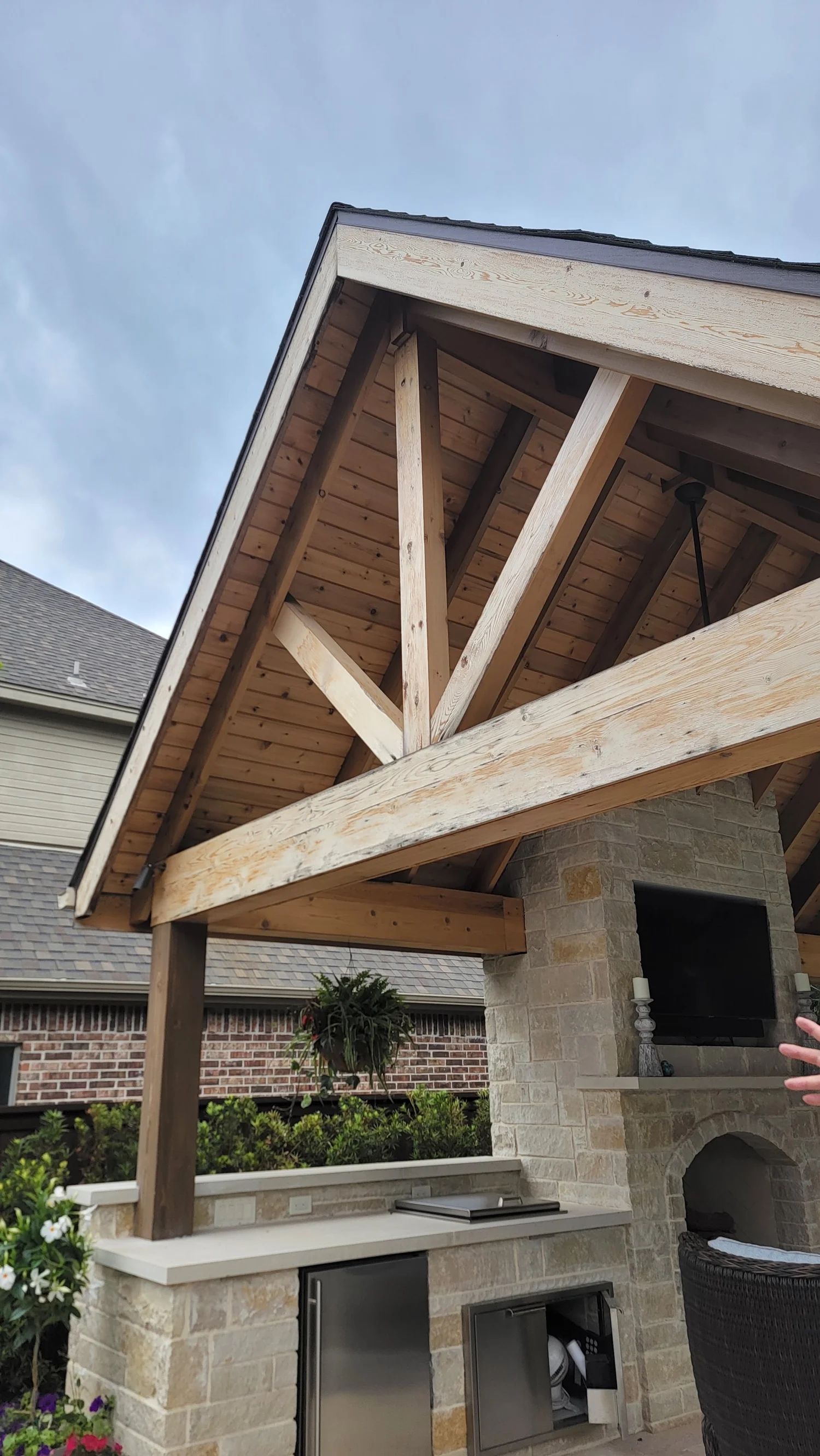 Outdoor kitchen with wooden truss roof and stone facade.