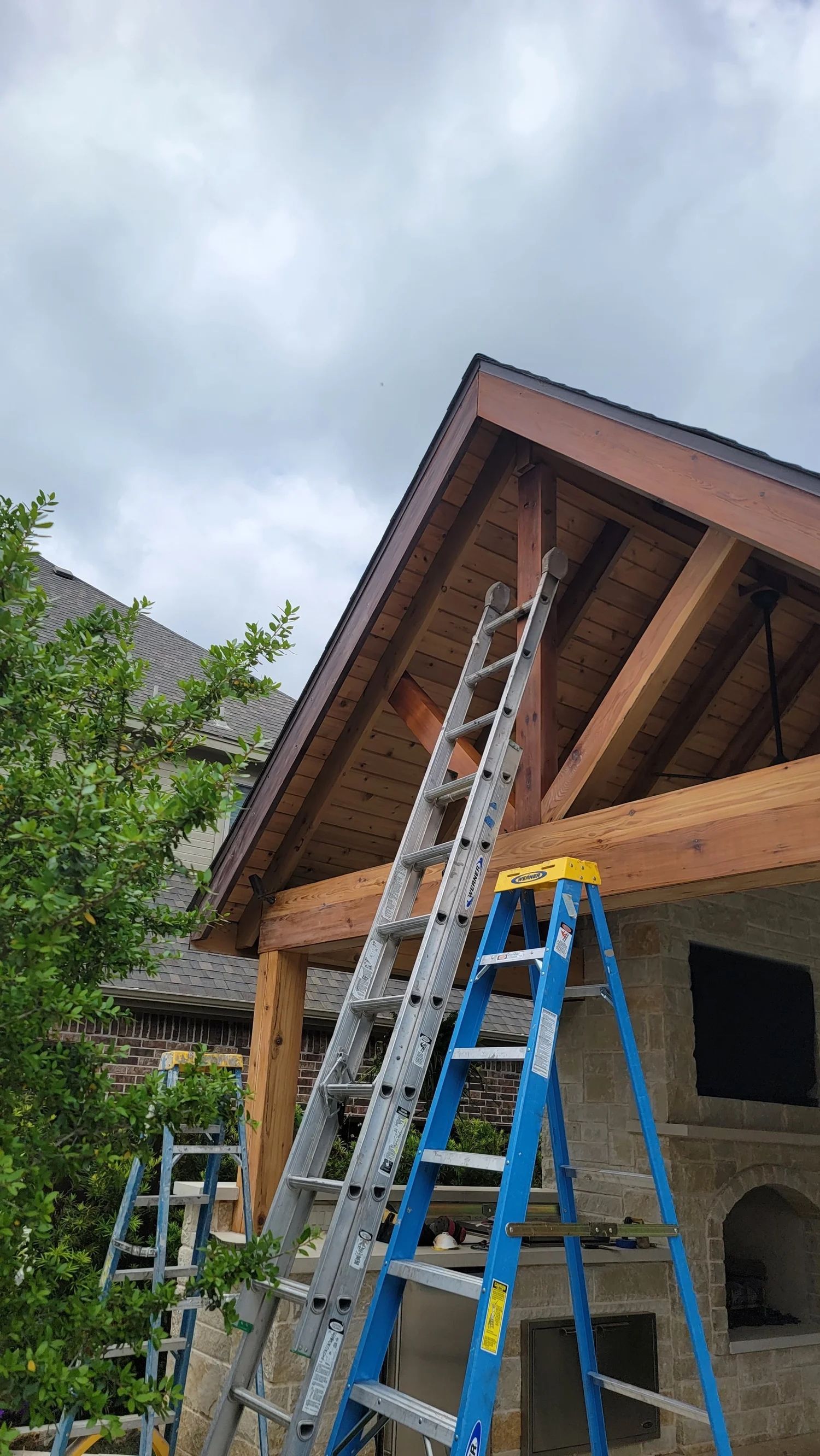 Two ladders against a roof with exposed wooden beams, cloudy sky.