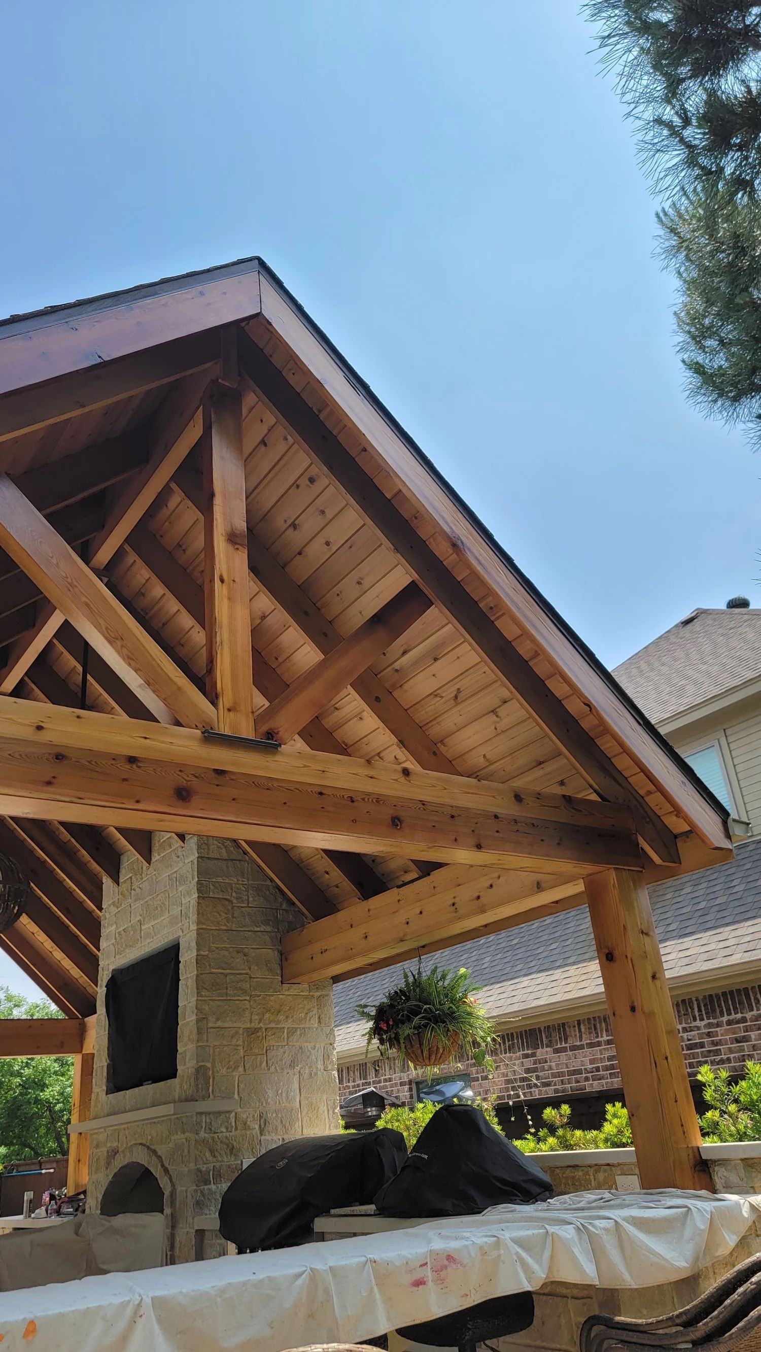 Wooden pergola with fireplace, under a blue sky.