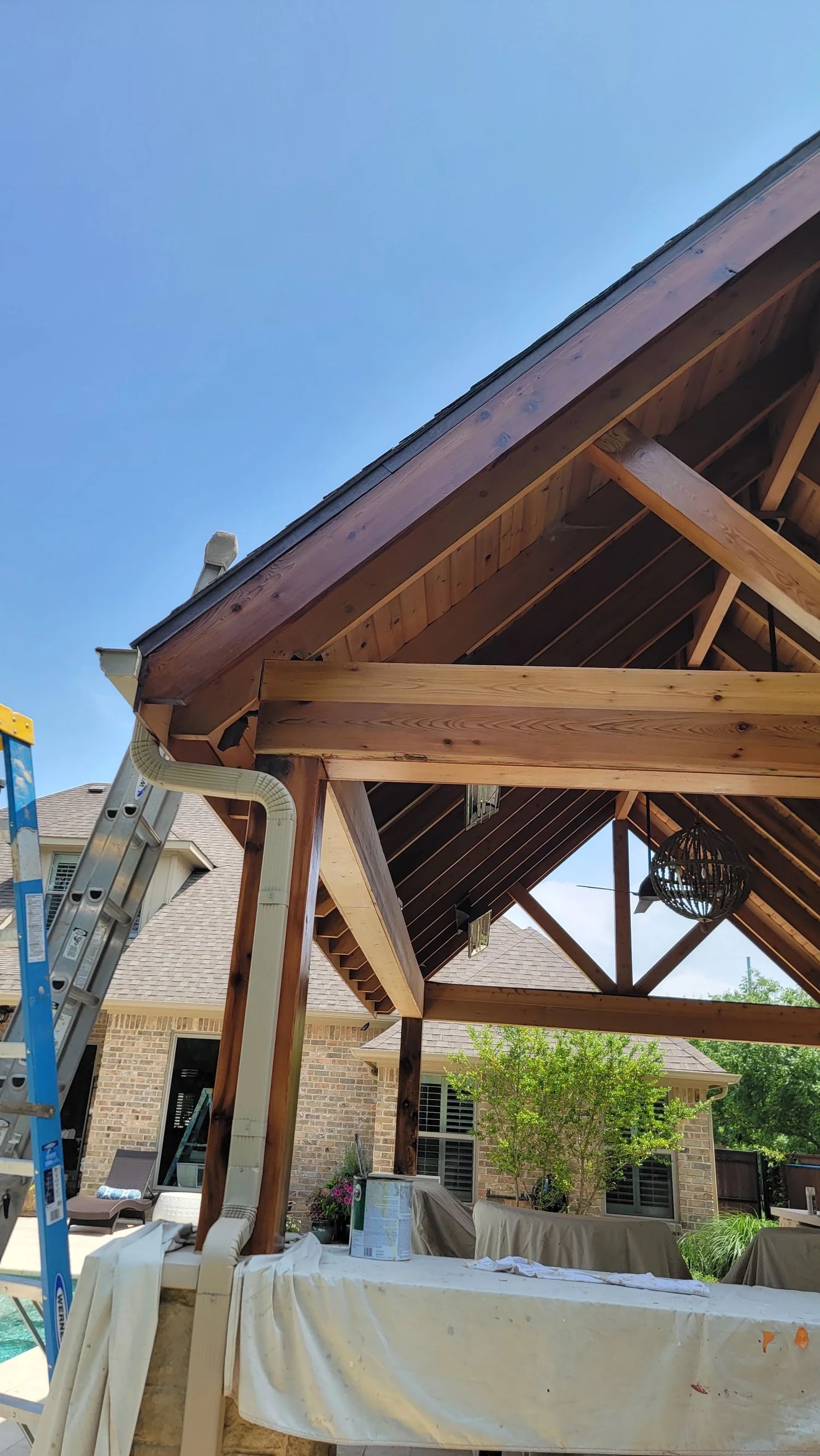 Wooden patio roof with gutter, against a blue sky, near a house and swimming pool.
