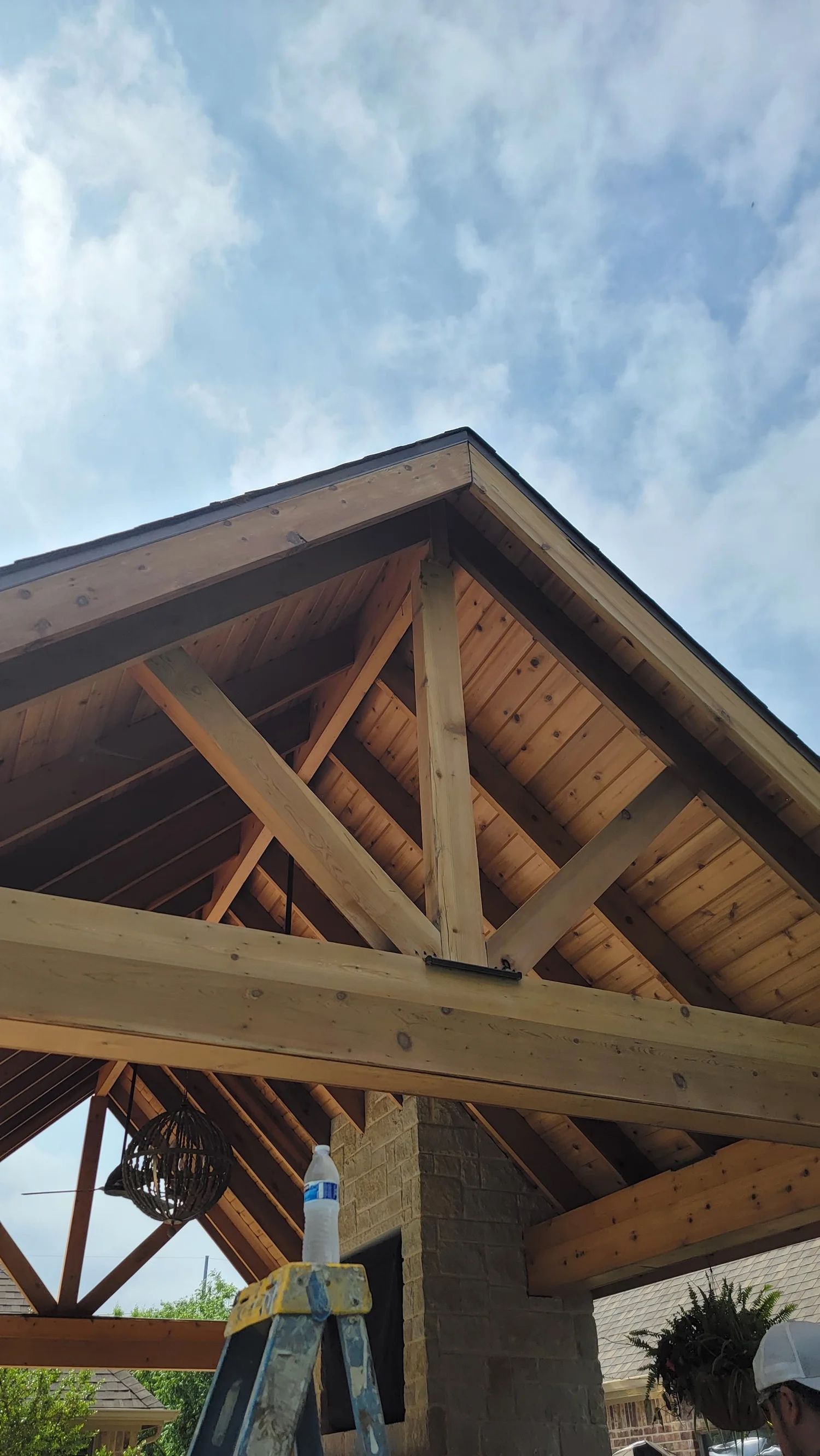Wooden roof of a structure with interior support beams against a cloudy sky.