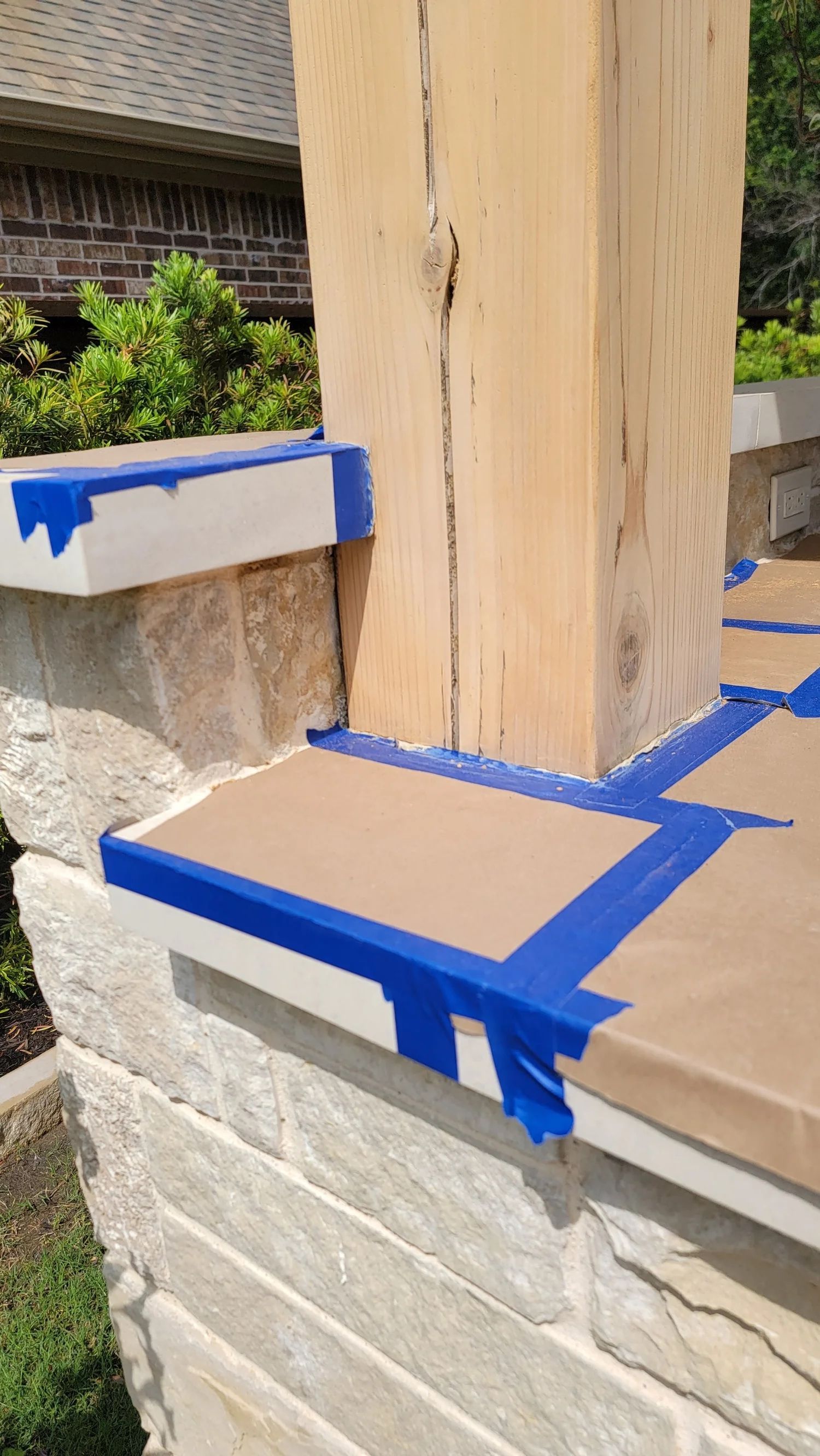 Stone pillar with blue painter's tape along edges, preparing for painting or staining.