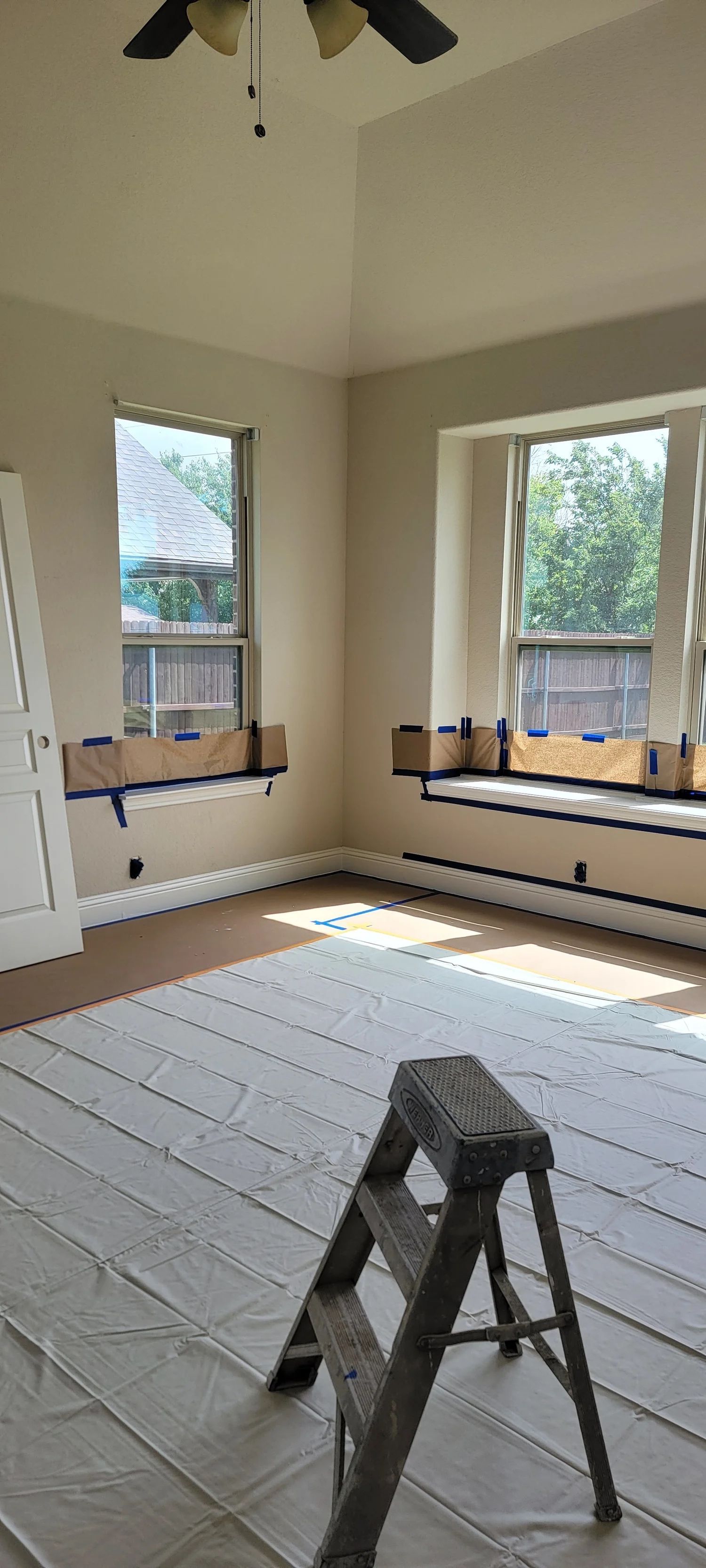 Room interior under construction with windows, ladder, and floor covering.