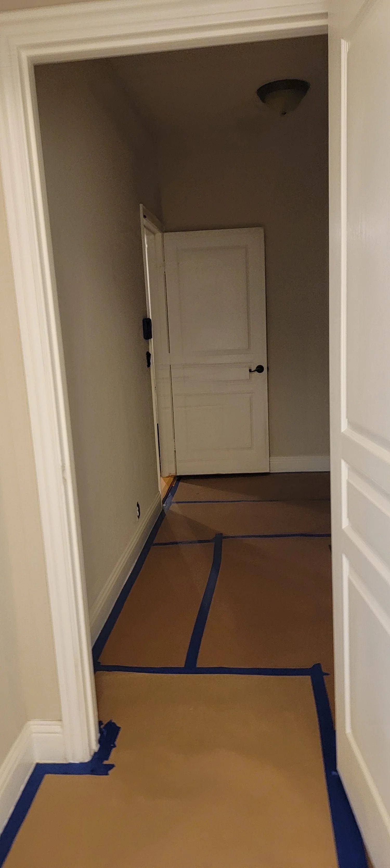 A hallway with a white door at the end, covered with cardboard and blue painter's tape.