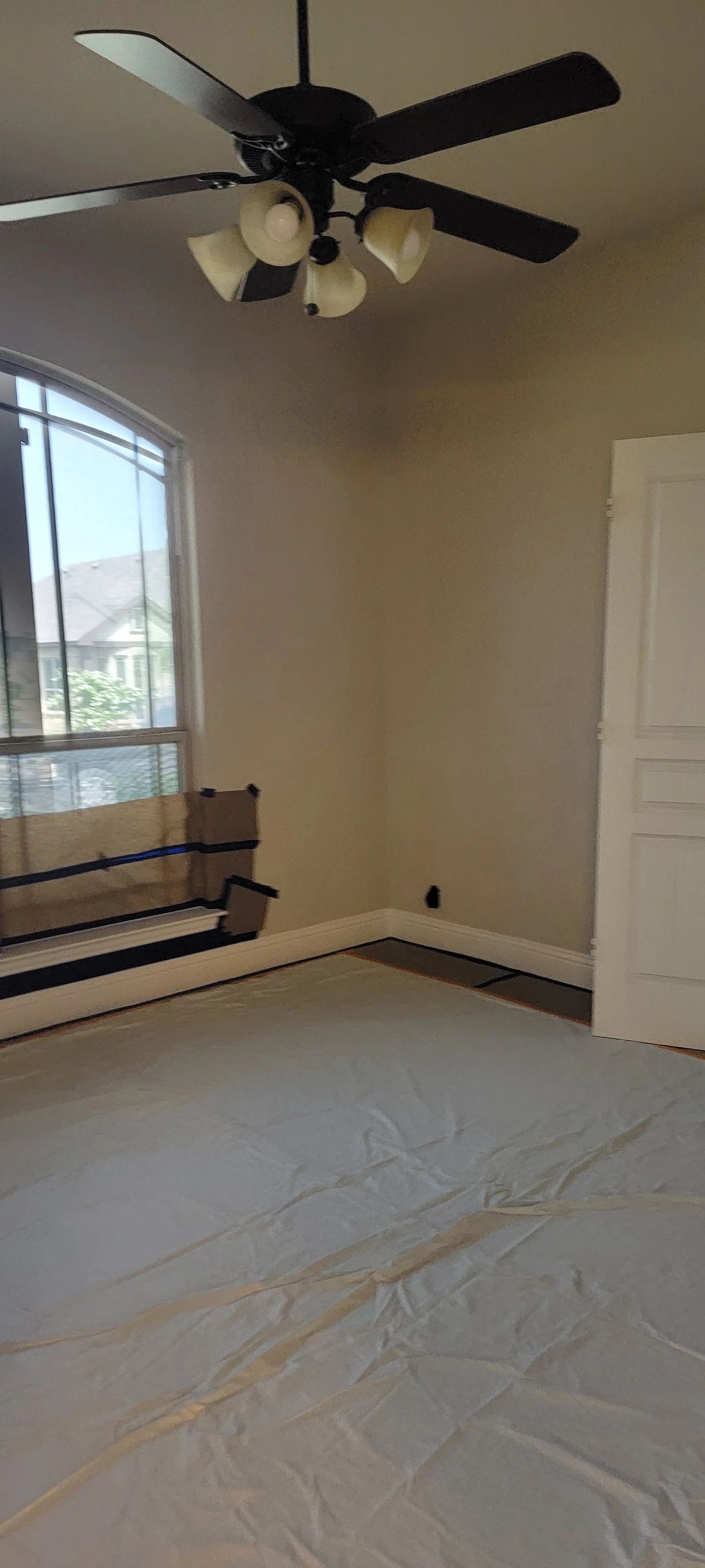 A room with a ceiling fan, a window, and a door, protected by a floor covering.