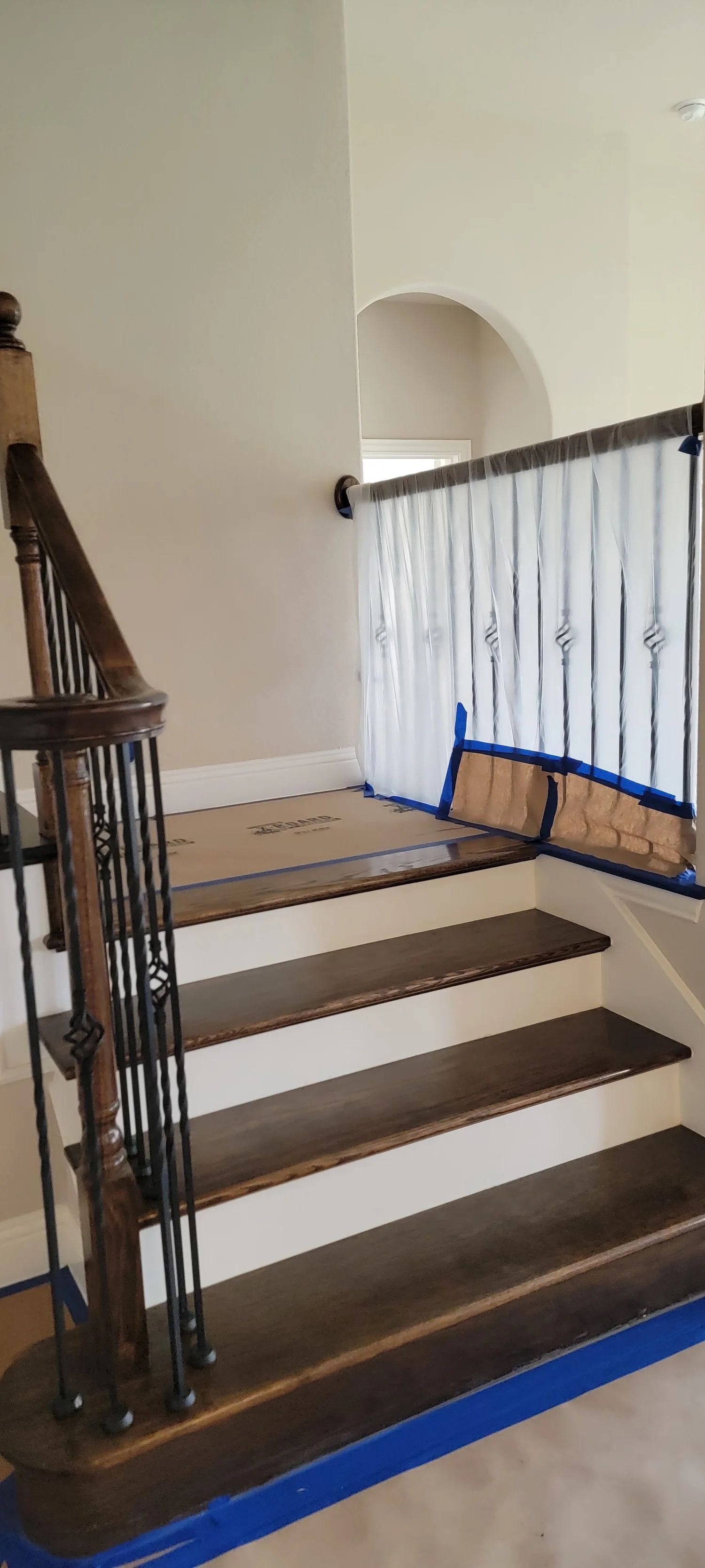 Wooden staircase with dark brown treads and black iron railings, blue tape on floor.