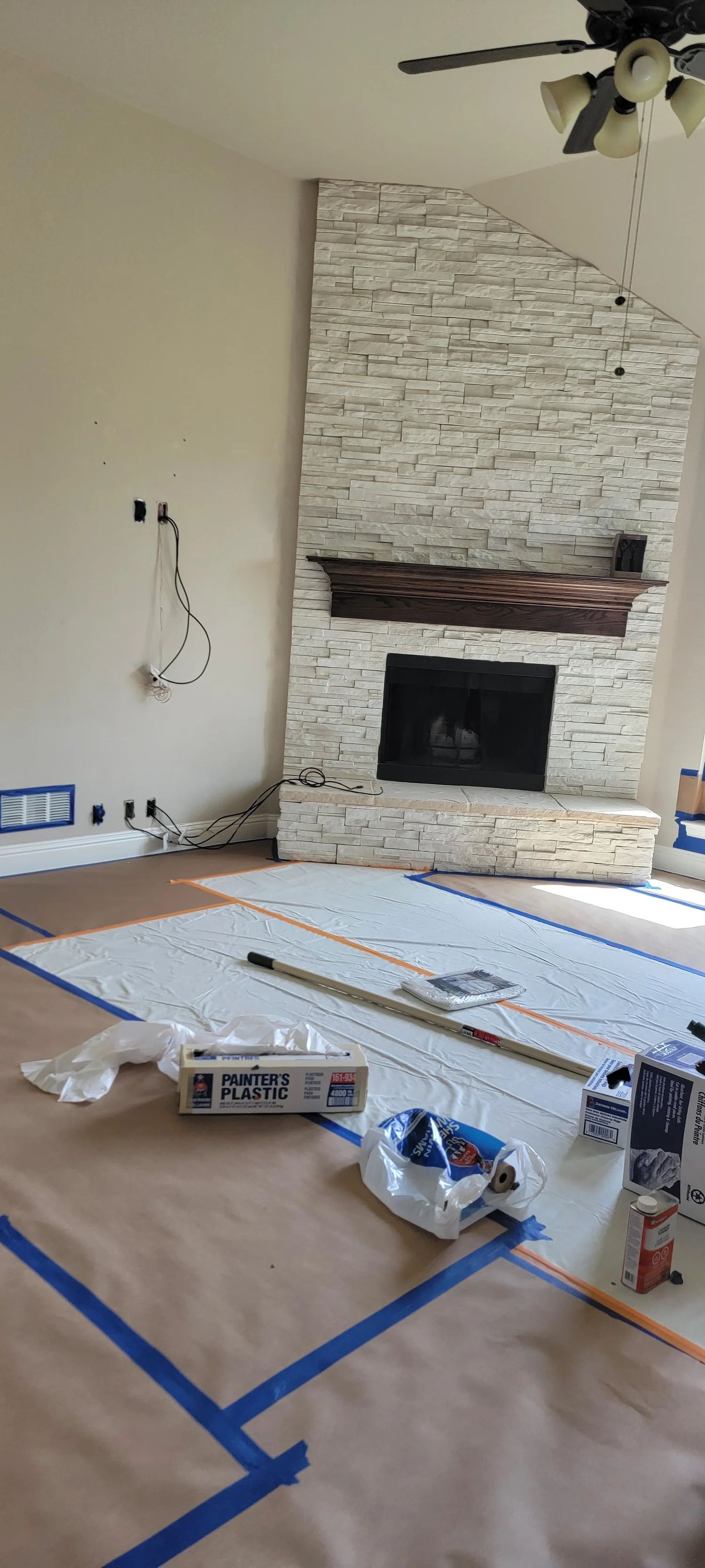 Room with fireplace being renovated, covered floor, tools visible.