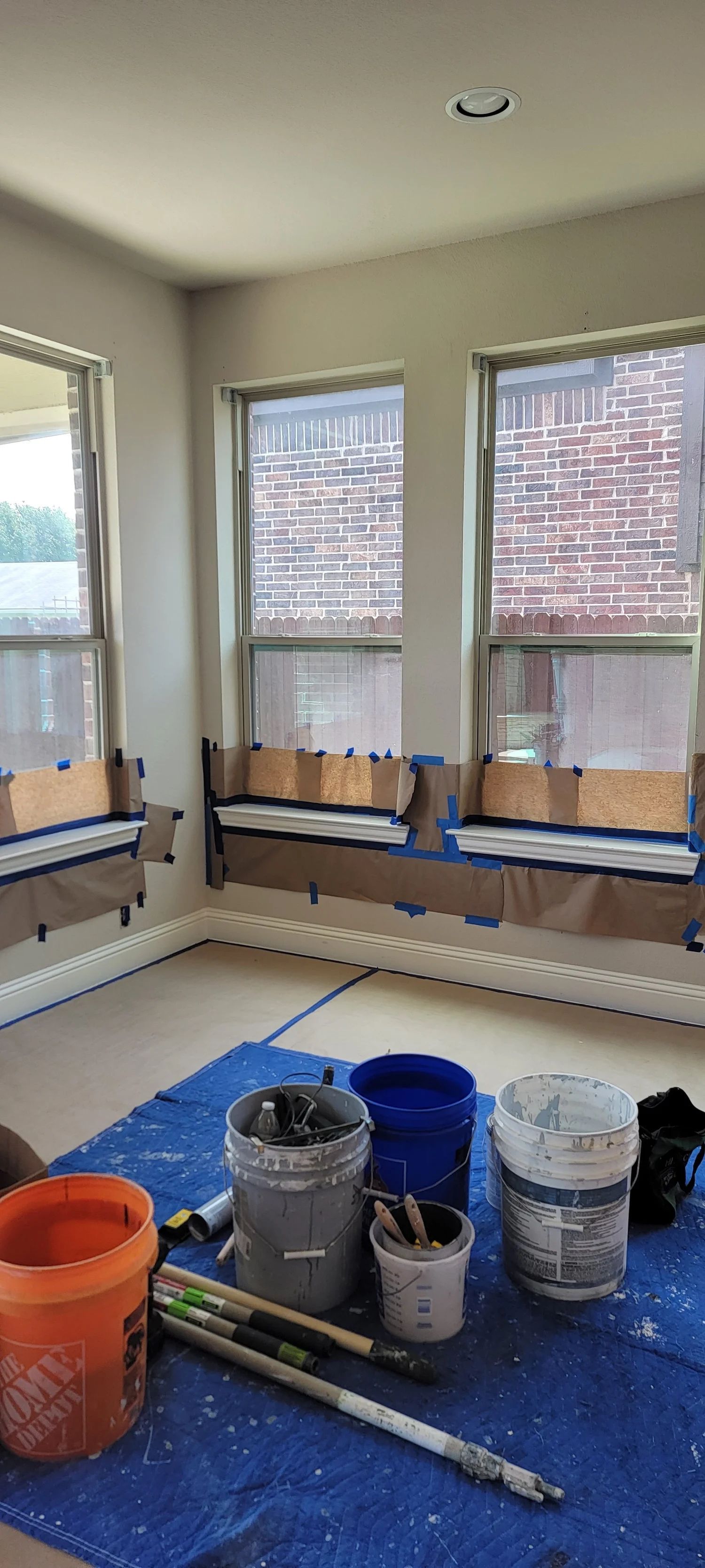 Room prepared for painting; windows covered, paint buckets, brushes on blue tarp.