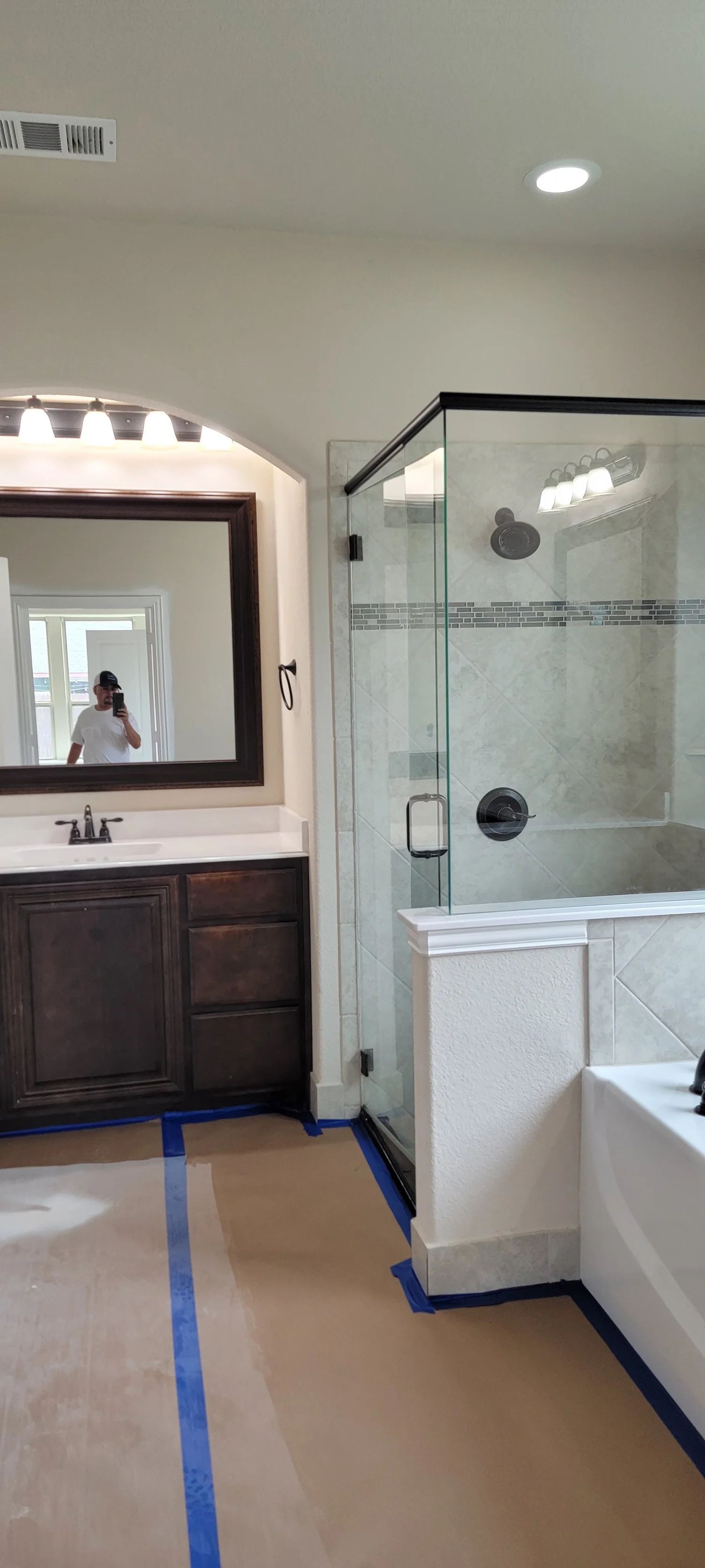 Bathroom with dark wood vanity, glass shower, and tub. Blue tape protects the floor during construction.