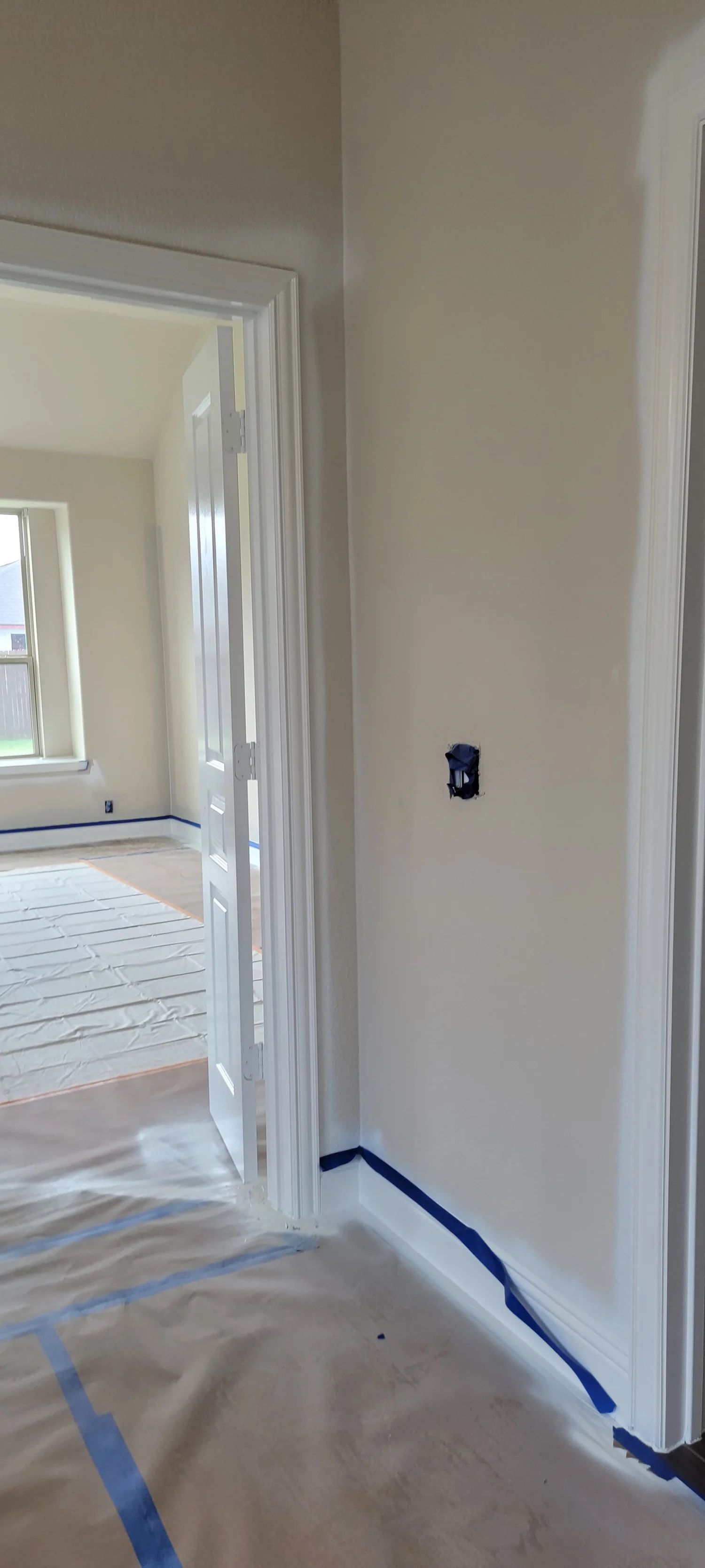 Interior shot of a room with painted walls and masking tape along the baseboards; doorway visible.