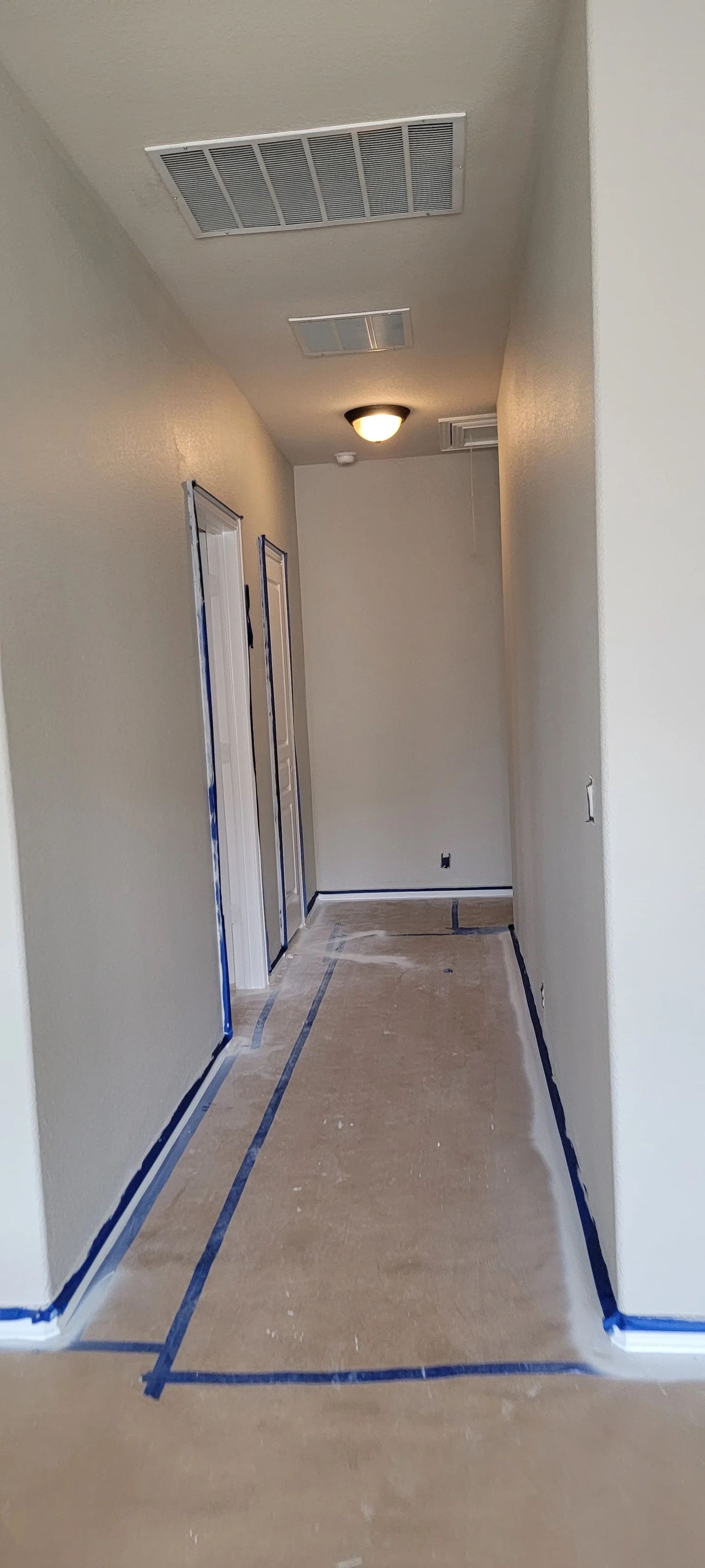 Hallway with fresh paint, blue tape, and a vent.