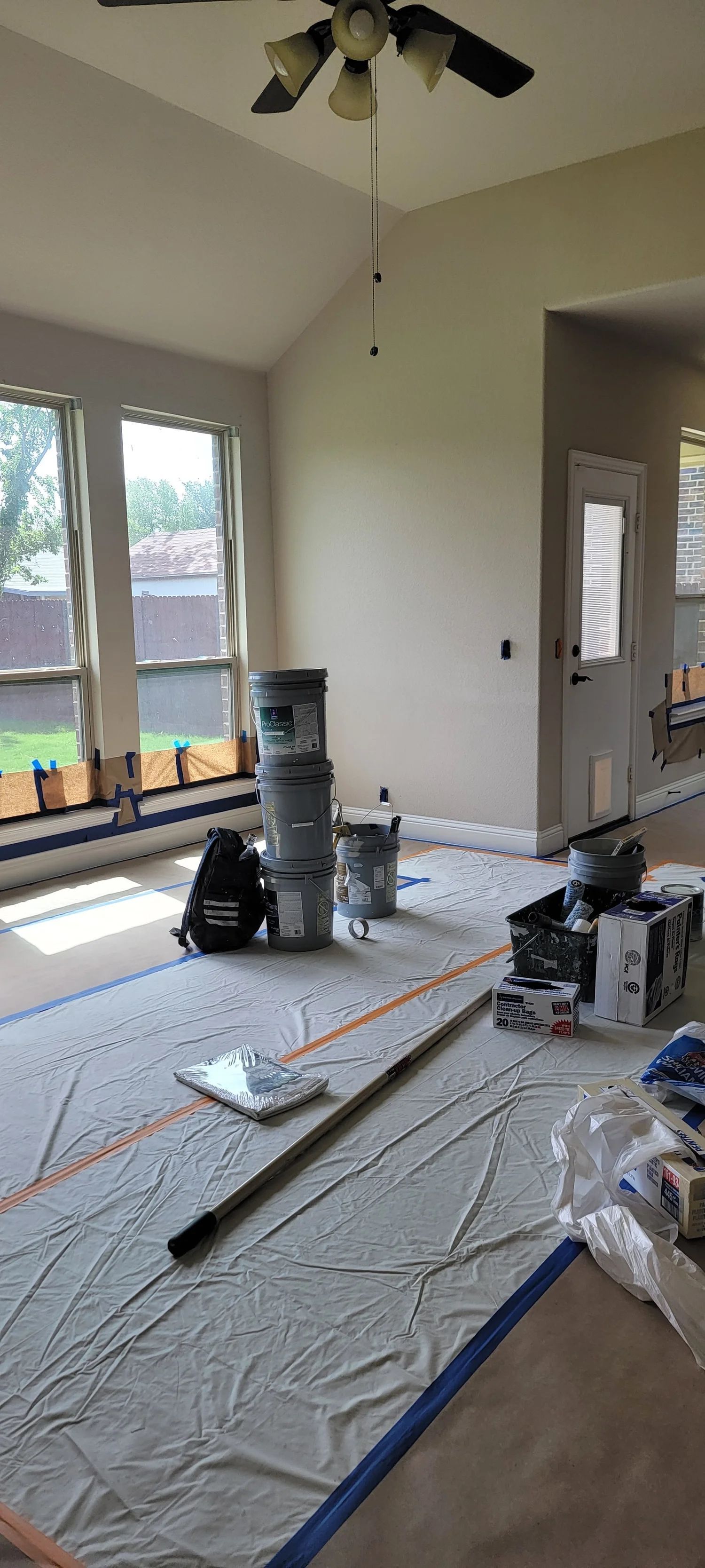 Room being prepped for painting: paint buckets, drop cloths, tape, and tools cover the floor.