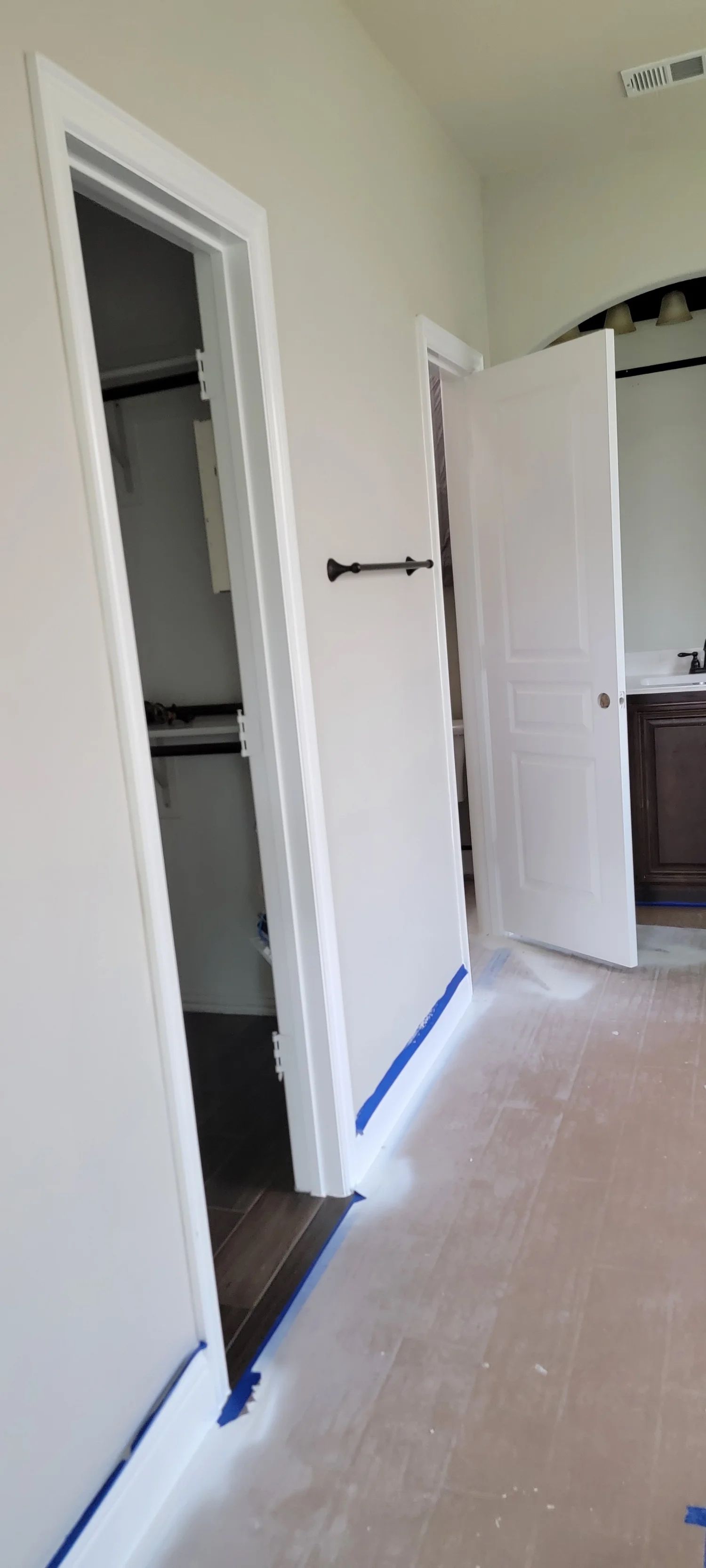 A room with two doors and a closet. One door is open. White paint with blue tape on the floor.