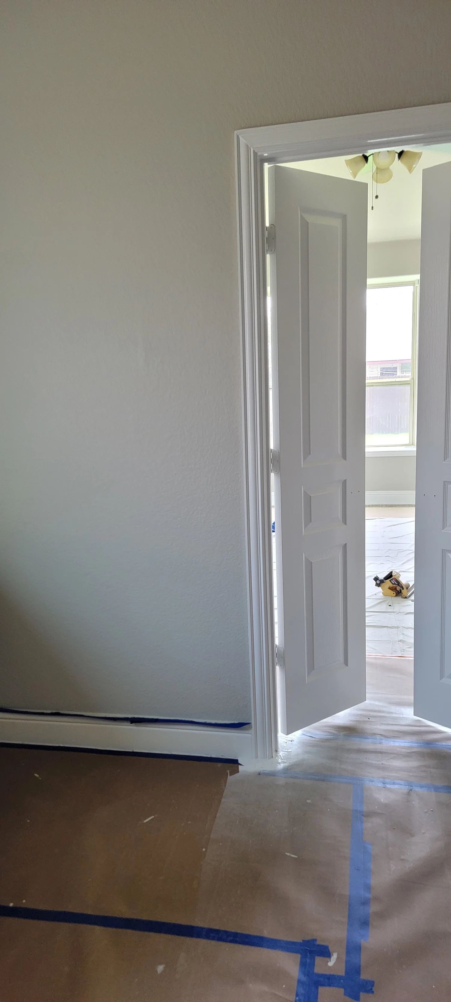 Interior of a room with white doors open. Light streams into the room. Brown paper covers the floor.