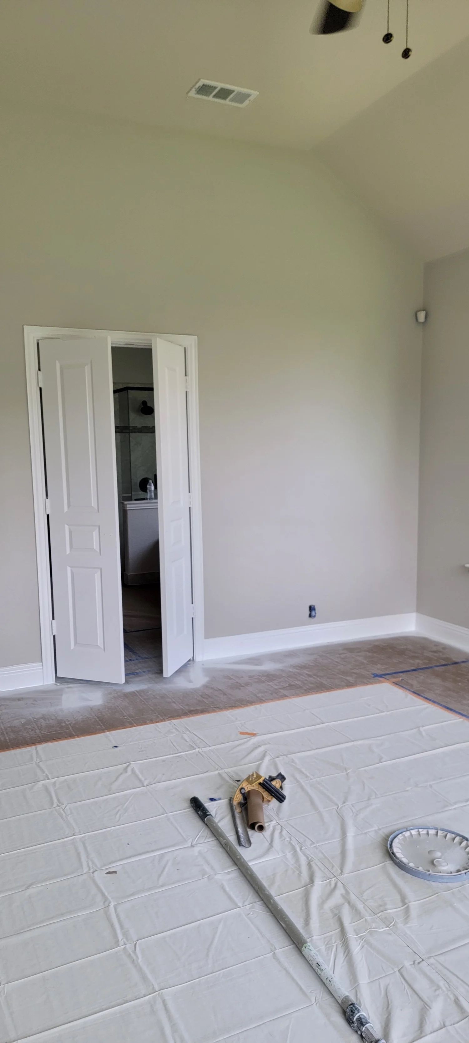 Interior room with white doors, paint supplies, and drop cloths on the floor.