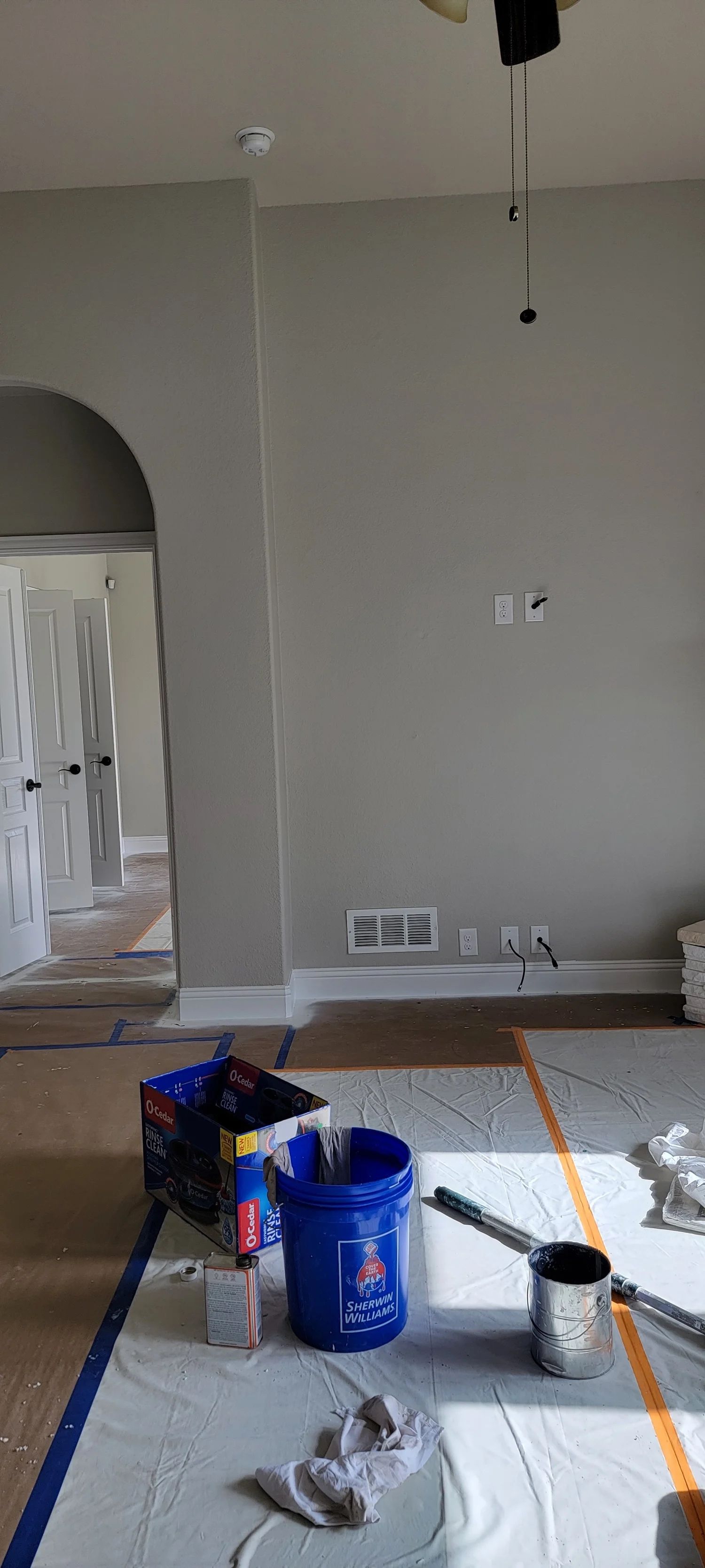 Room interior with painting supplies on drop cloths, partially painted walls.