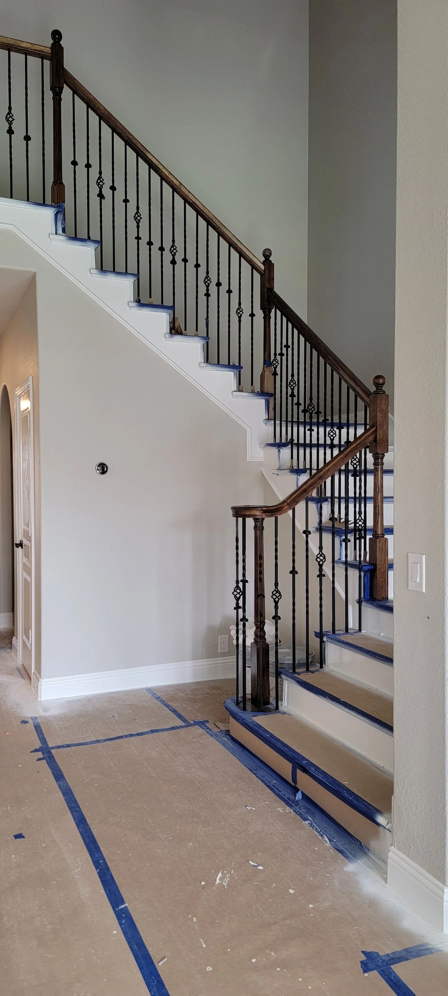 Interior view of a wooden staircase with black metal balusters and brown railing. Construction in progress.
