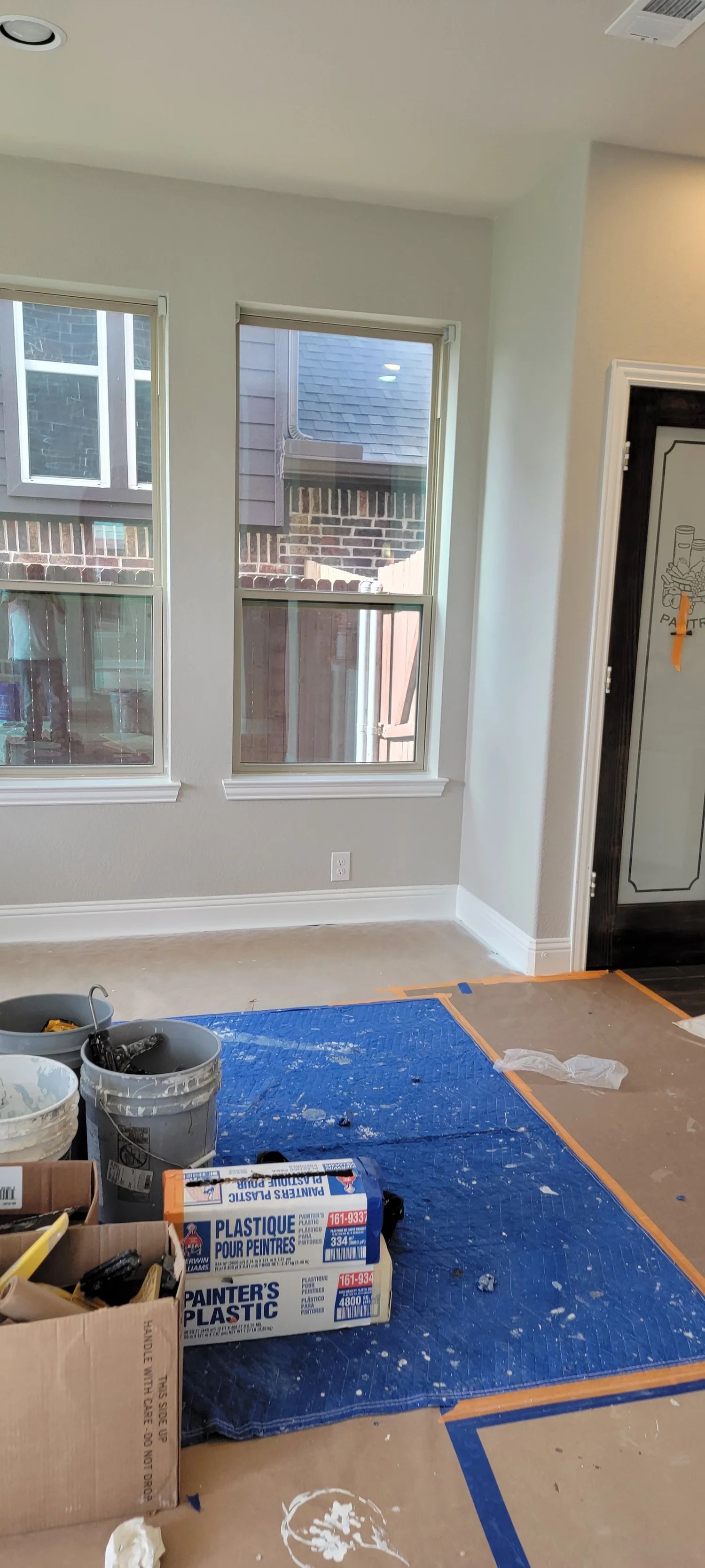 Interior room with two windows, work in progress. Blue tarp on floor, tools, and cardboard boxes.
