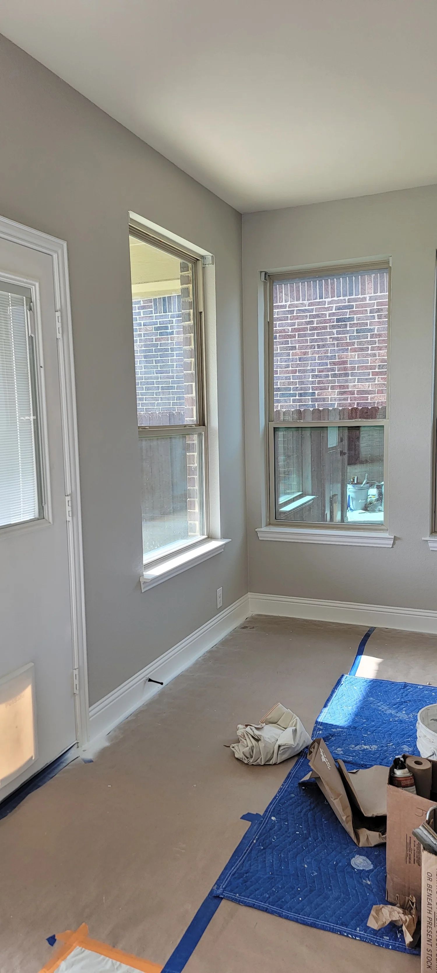 Interior view of a room with windows and light gray walls. Protective covering on the floor.