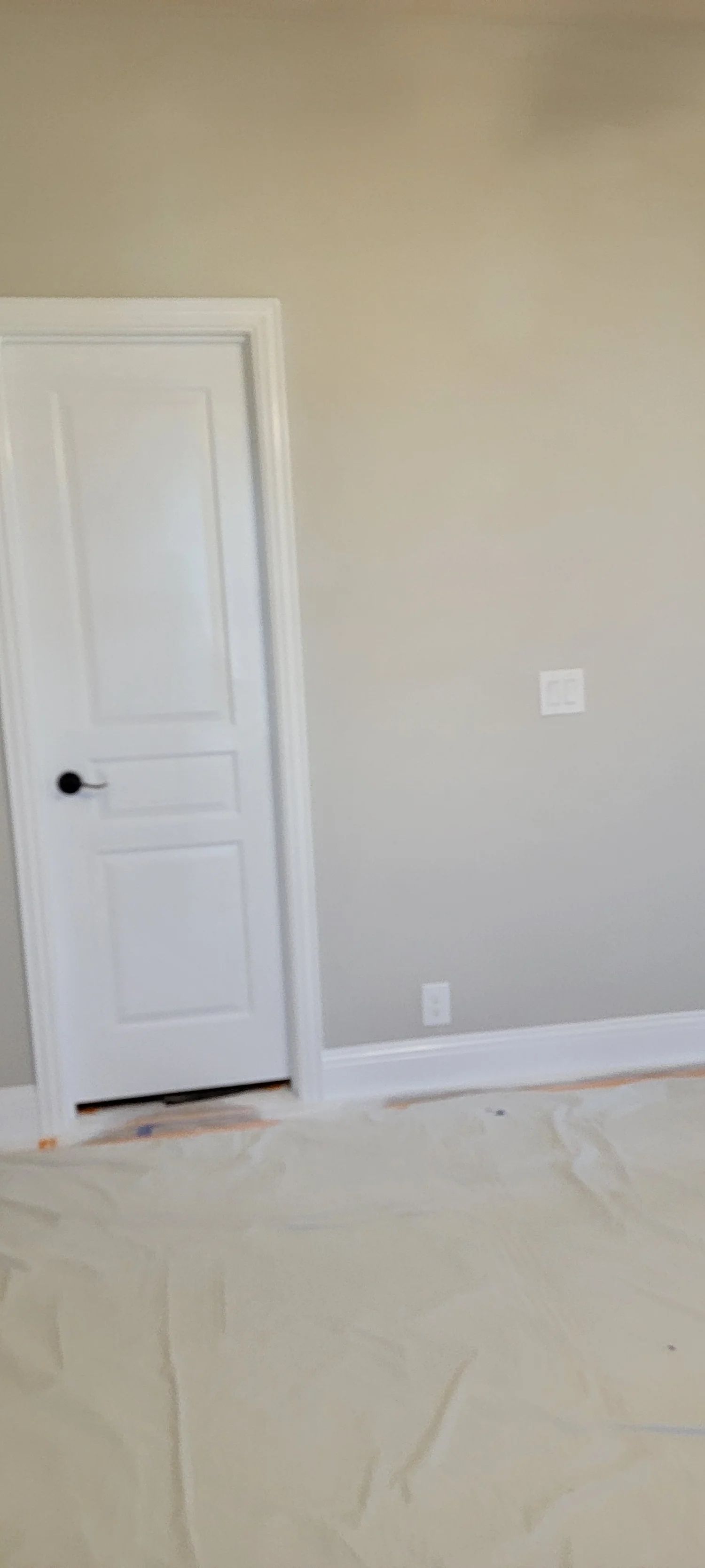 White door with black handle in room with light gray walls and protective floor covering.