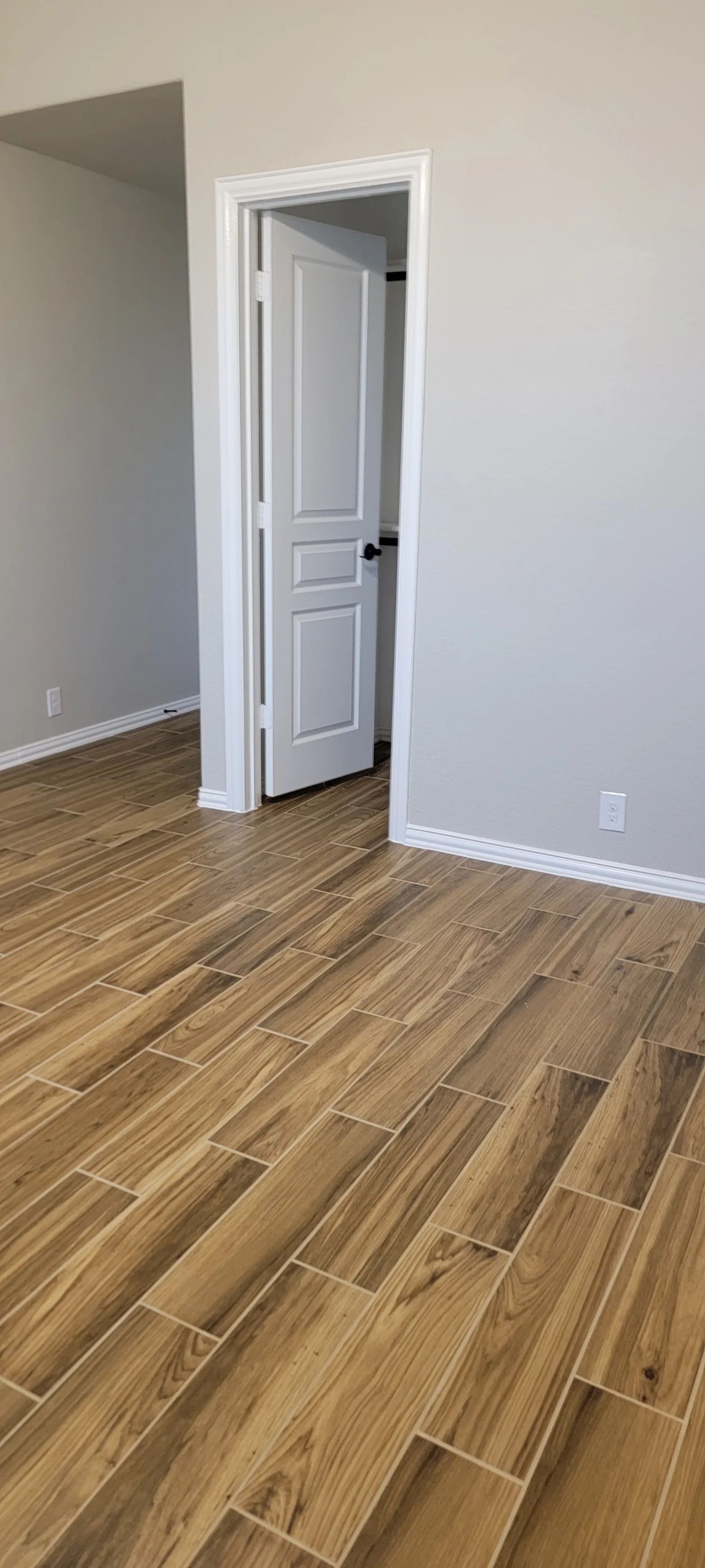 Room with wood-look tile flooring, gray walls, and an open white door.