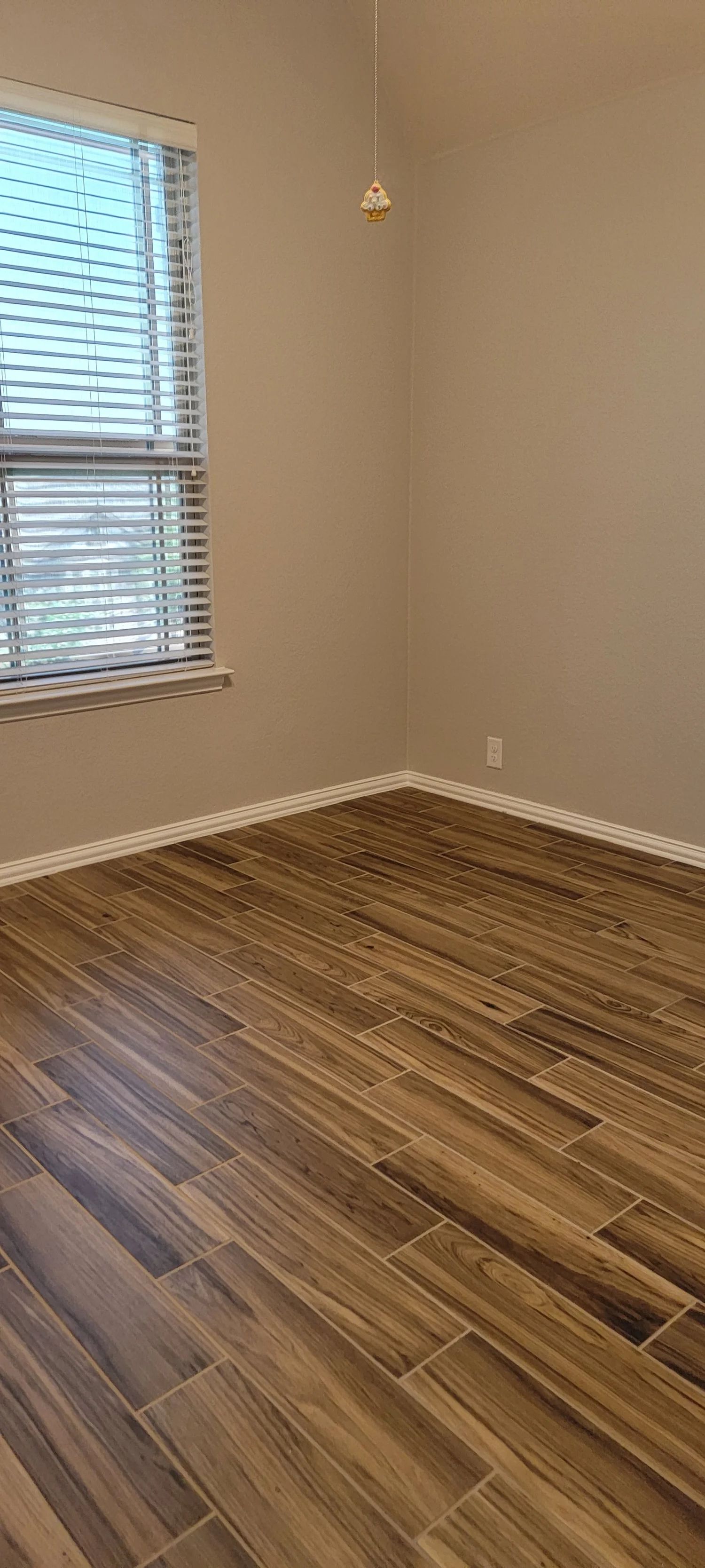 Empty room with wood-look floor, tan walls, and a window with blinds.