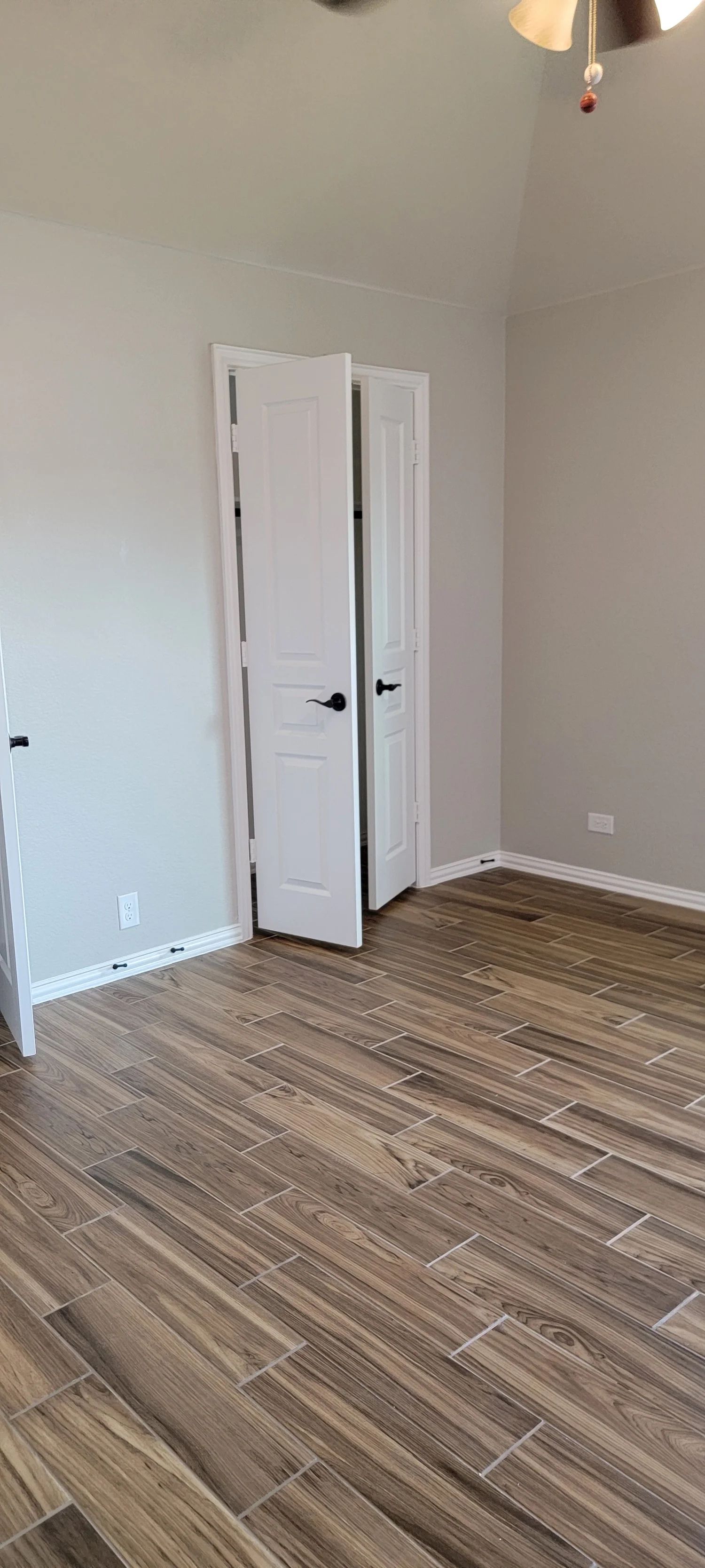 Room with wood-look tile floor and closed white doors. Gray walls, ceiling fan visible.