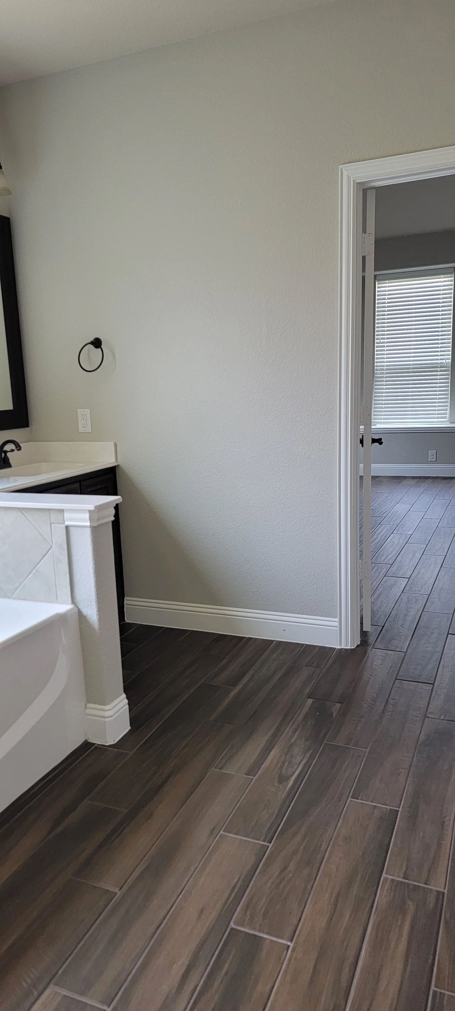 Bathroom interior with wooden floor, white trim, and a doorway leading to another room with blinds.
