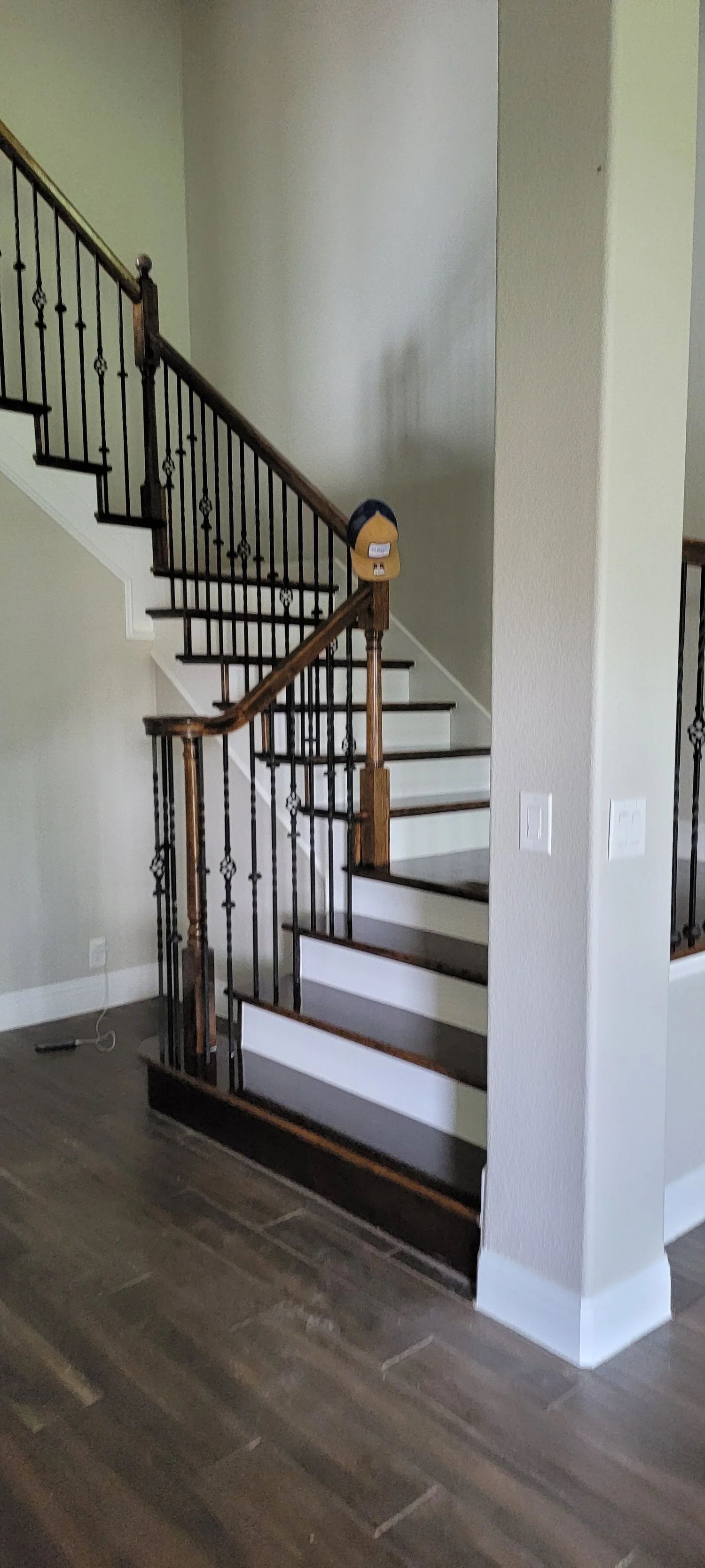 Staircase with wooden handrail and black iron balusters, ascending from a dark wood floor. White walls.