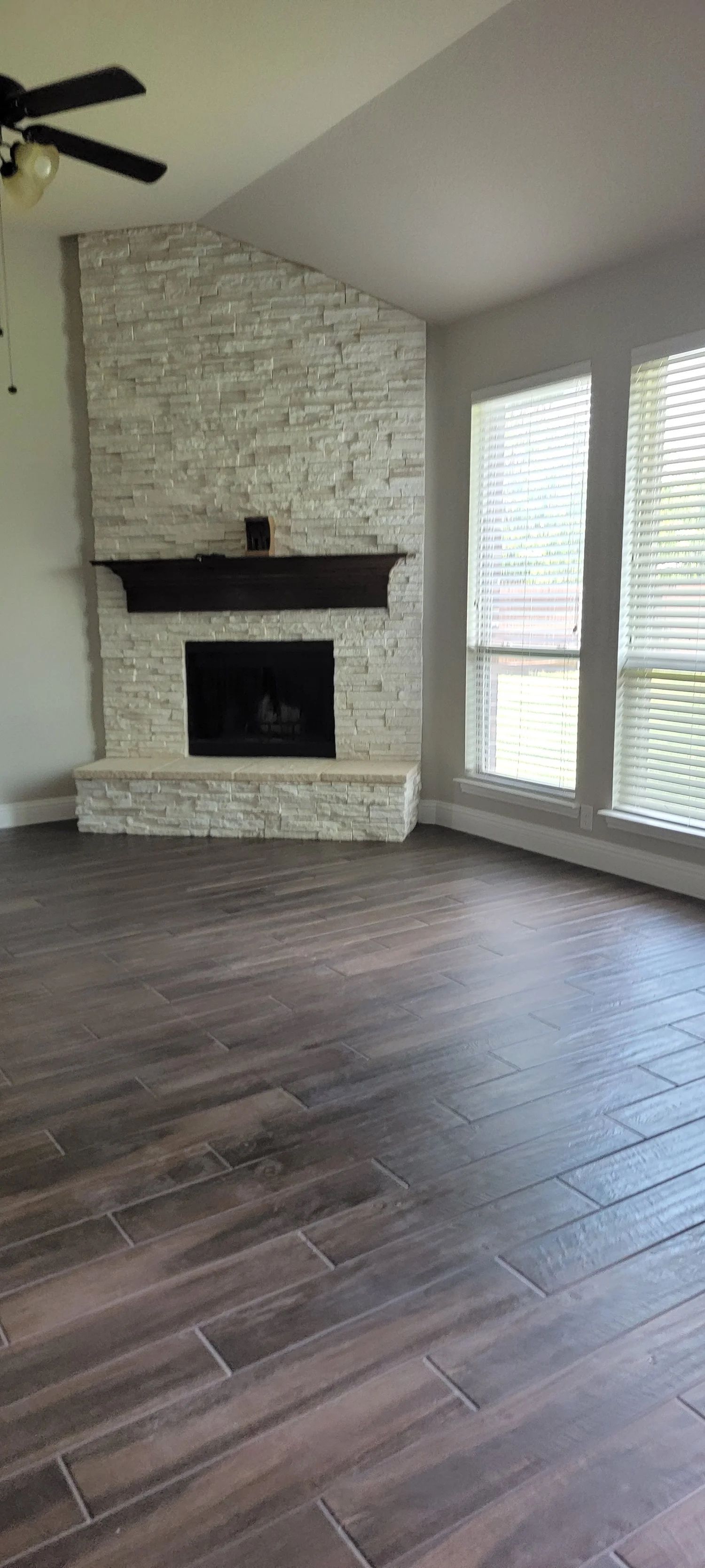Living room with fireplace and dark wood-look tile floor. Windows to the right.